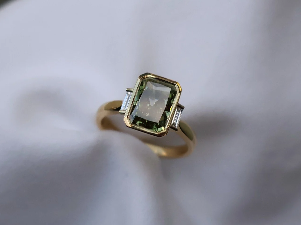 Radiant-cut green diamond and straight baguette three stone ring made in 18ct yellow gold
