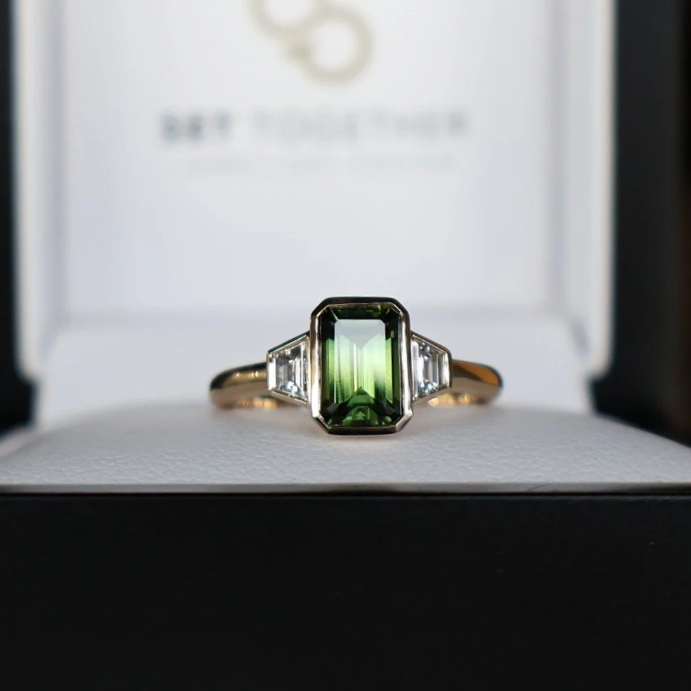 Emerald-cut green sapphire and trapezoid diamond three stone ring made in 14ct yellow gold