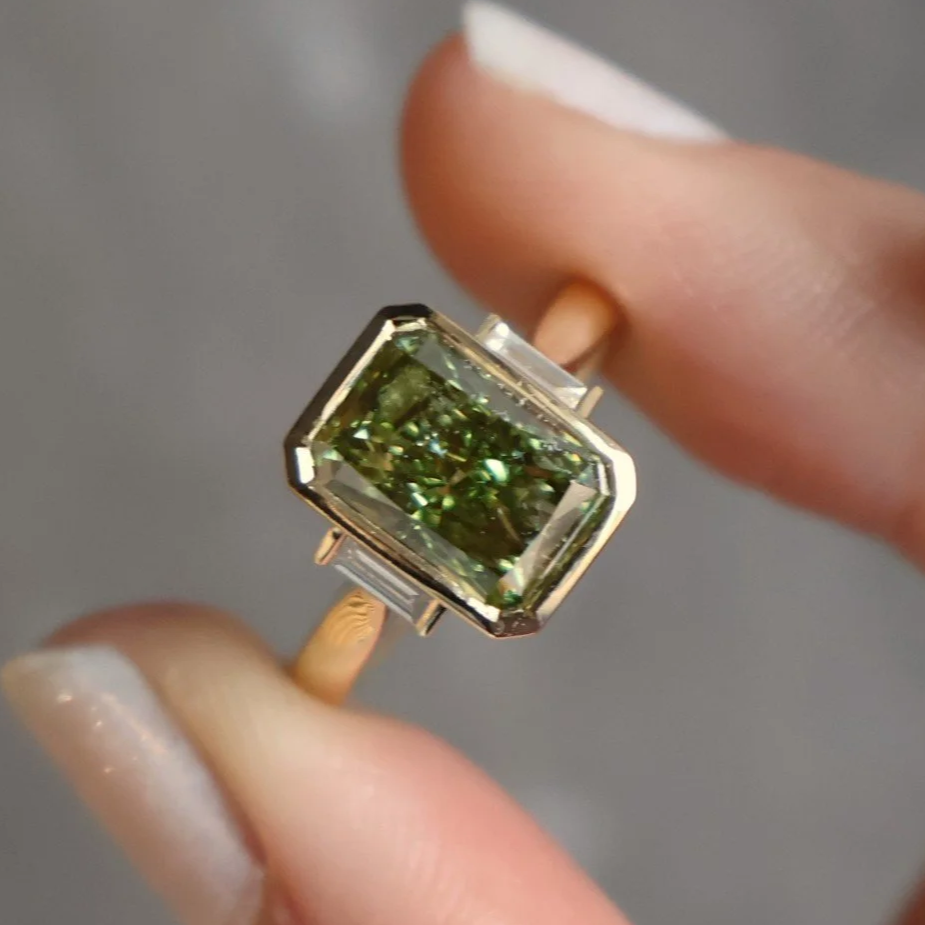 Green lab diamond radiant cut bezel set in an 18ct yellow gold ring with two small baguette diamonds either side