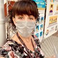 Woman with dark hair wearing a floral top and a face mask shopping at a store aisle with health products and informational posters in the background.