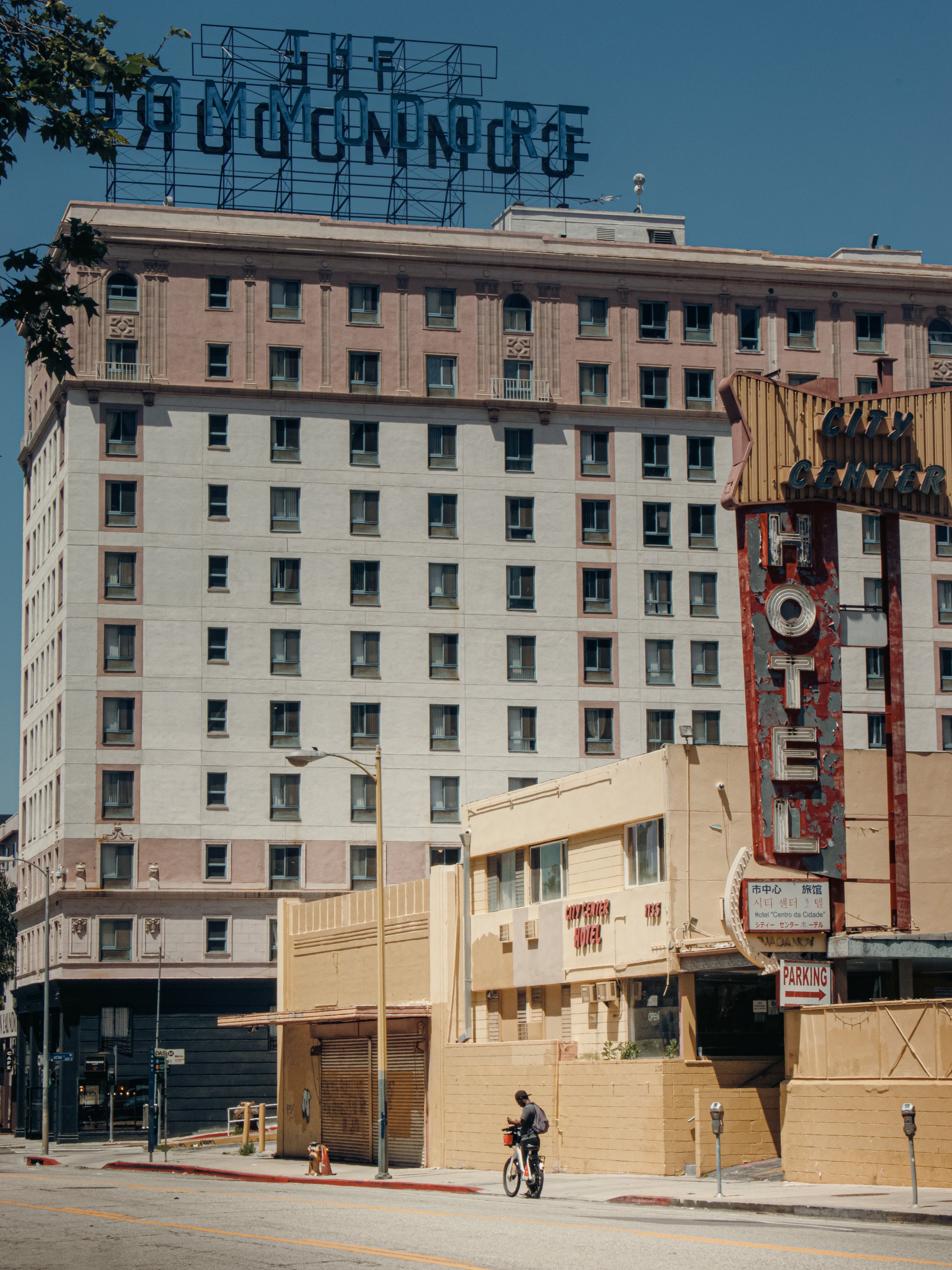 Vintage hotel buildings and retro signs in Los Angeles with a person cycling past in the midday sun.