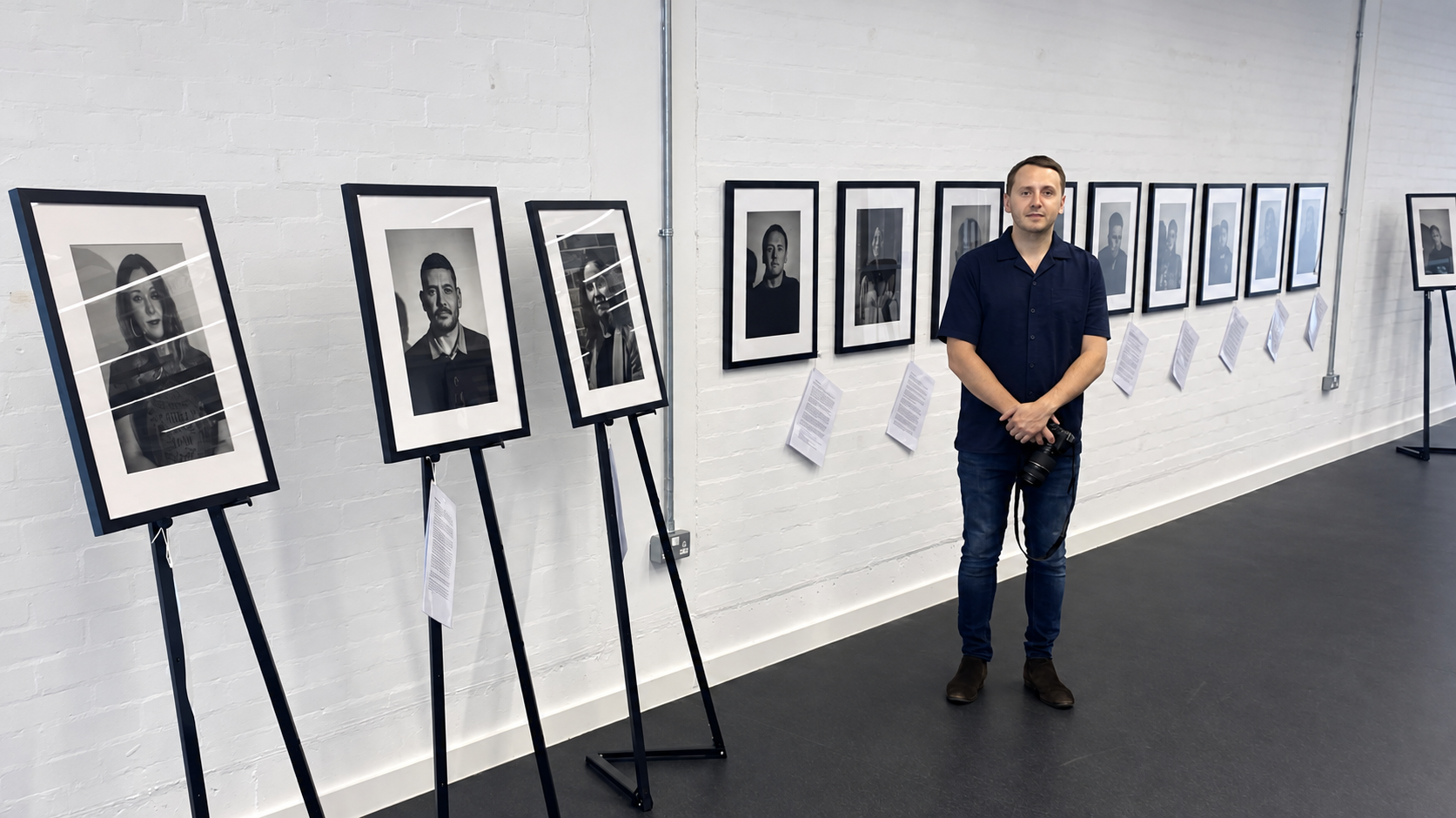 Photographer Lee Cooper standing beside Victorious Voices portraits displayed at Coventry University. View exhibitions.