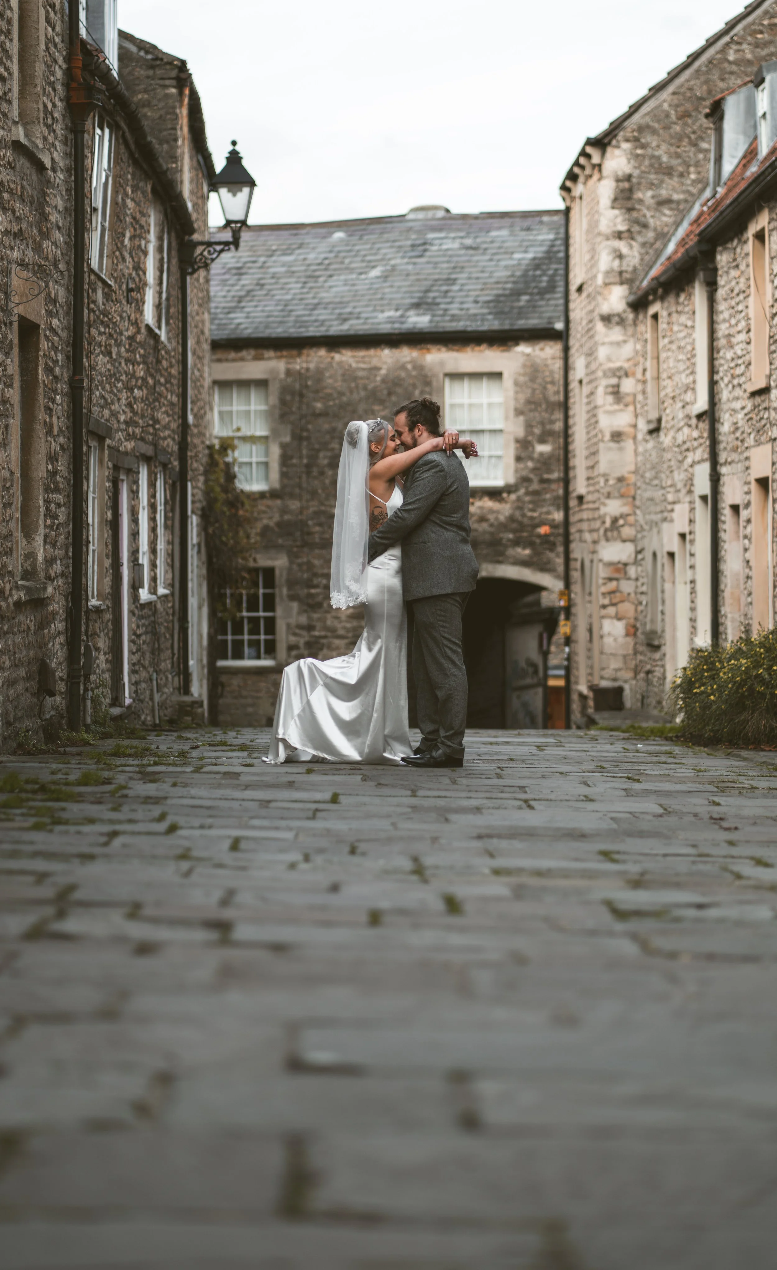Bride and groom embracing on a stone-paved street between rustic buildings