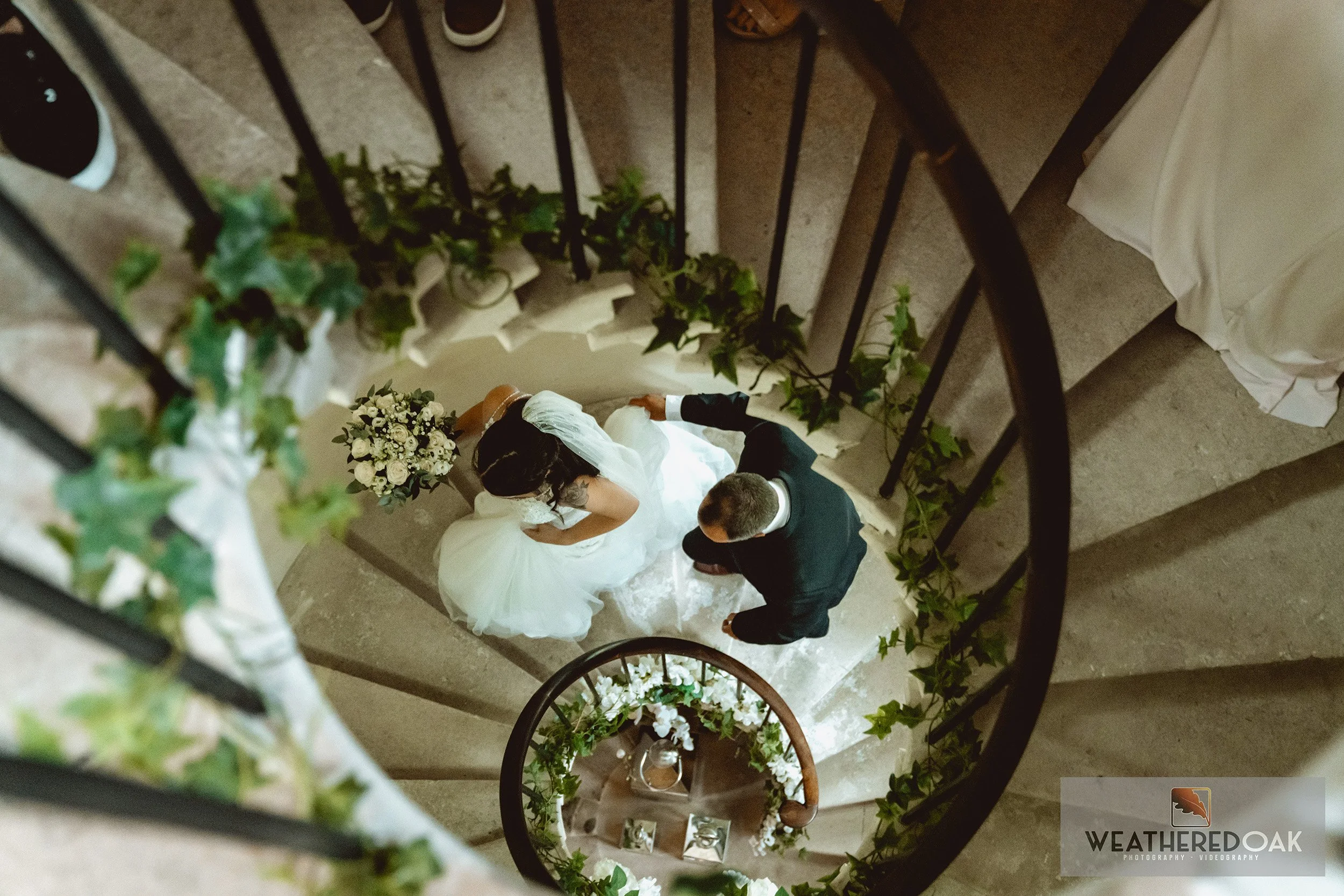 Overhead view of a bride and groom on a spiral staircase decorated with greenery and flowers.