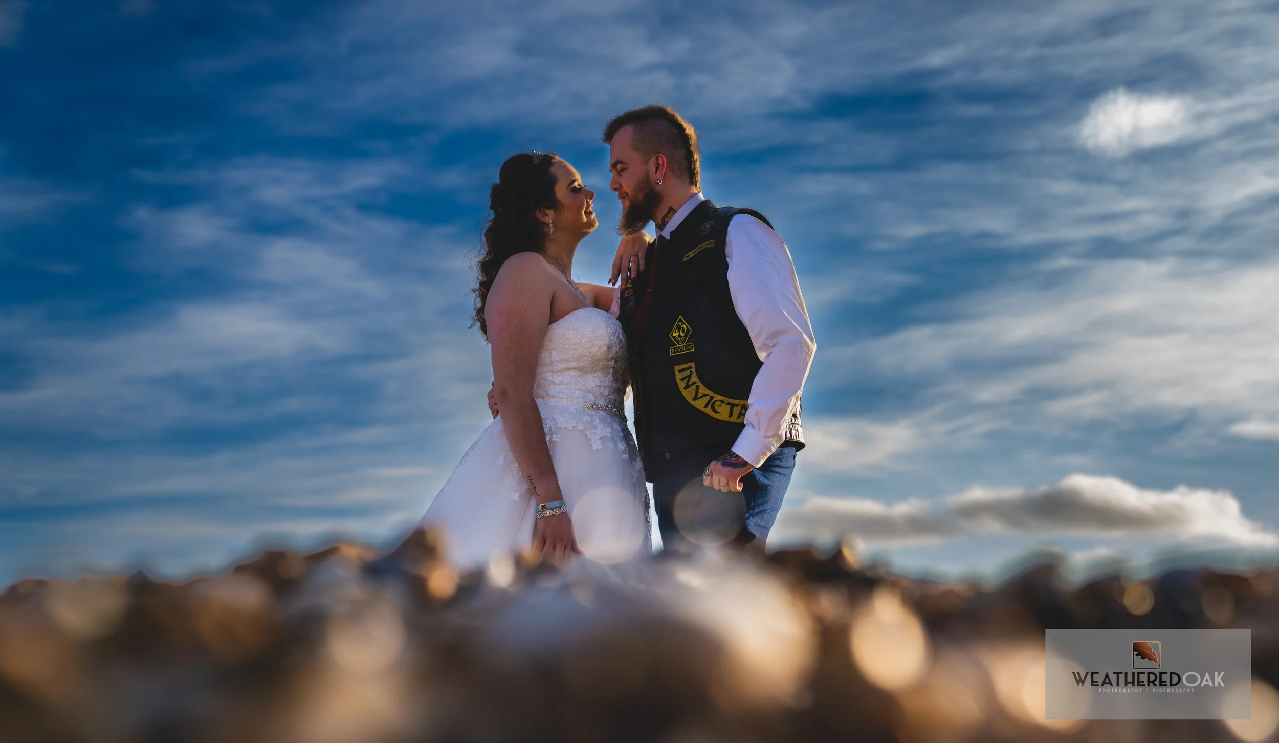 Bride and groom embracing outdoors against a blue sky.