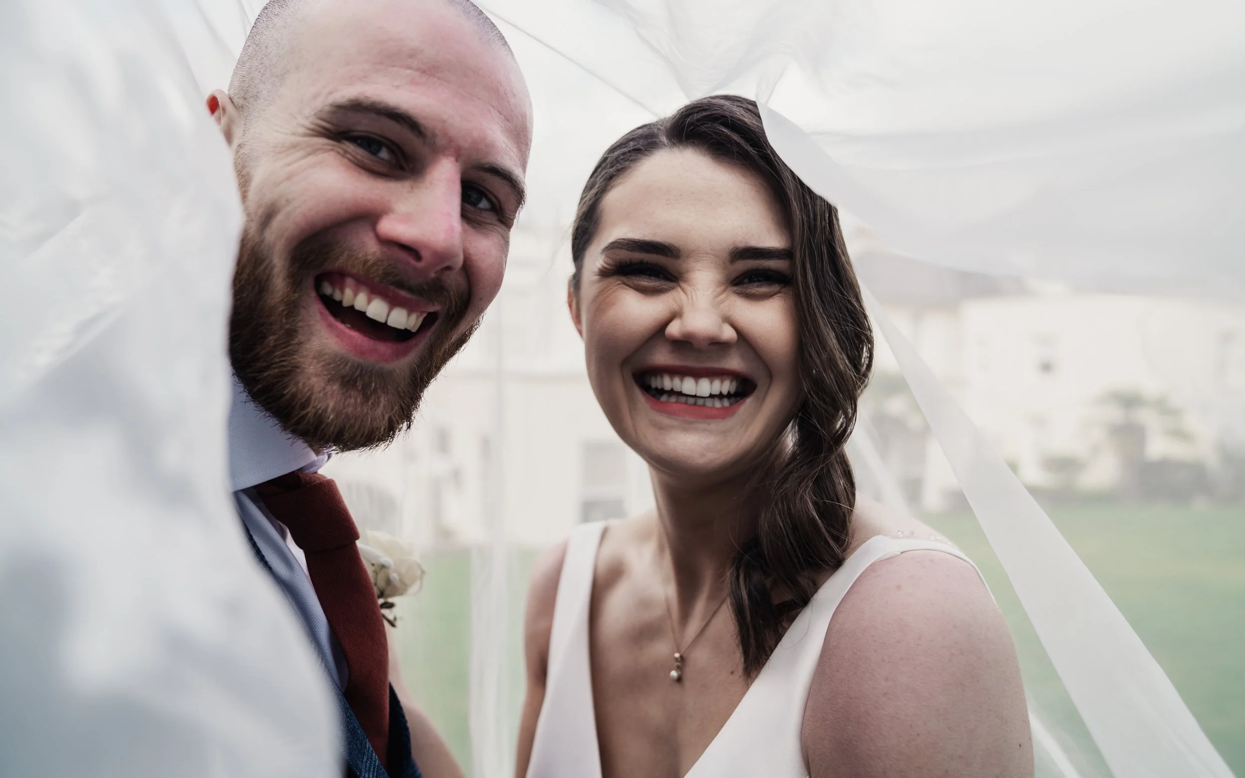 Smiling couple on their wedding day with a veil surrounding them.