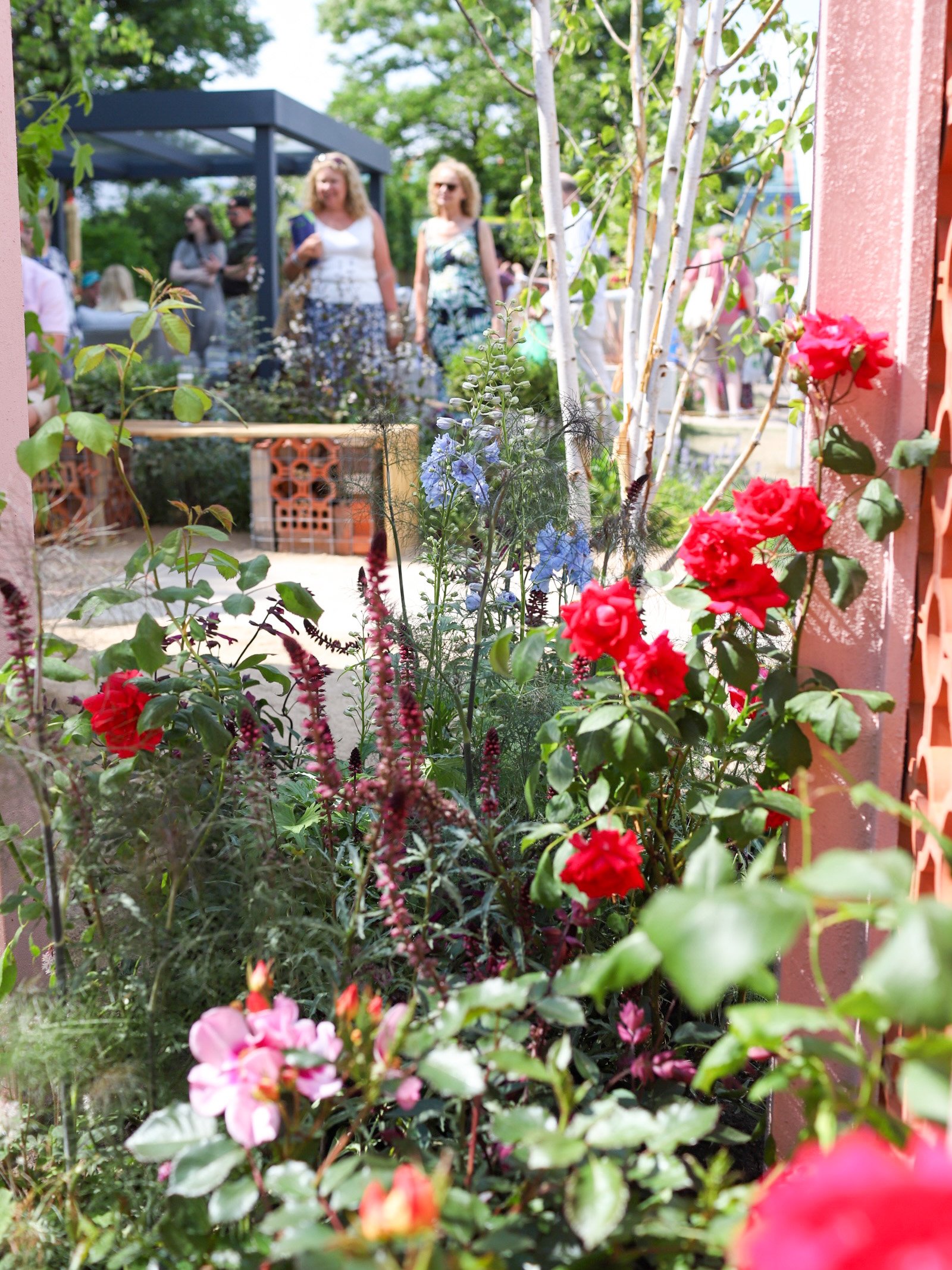 Two women looking at a garden with bright, colourful flowers , garden bench and gravel paths