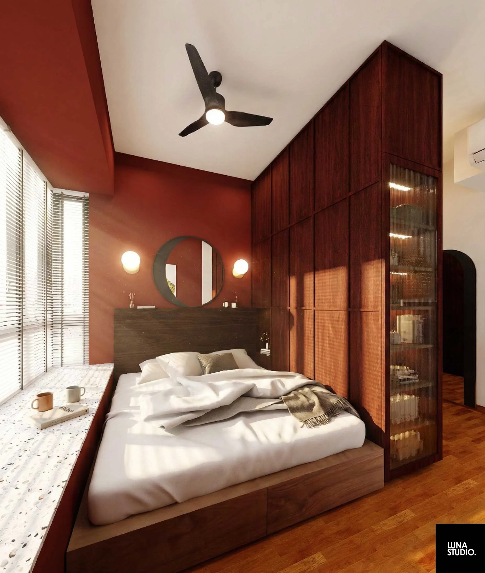 Modern bedroom with wooden accents, unmade bed with white linens, a circular mirror, two wall-mounted lights, blinds on windows, and a ceiling fan.