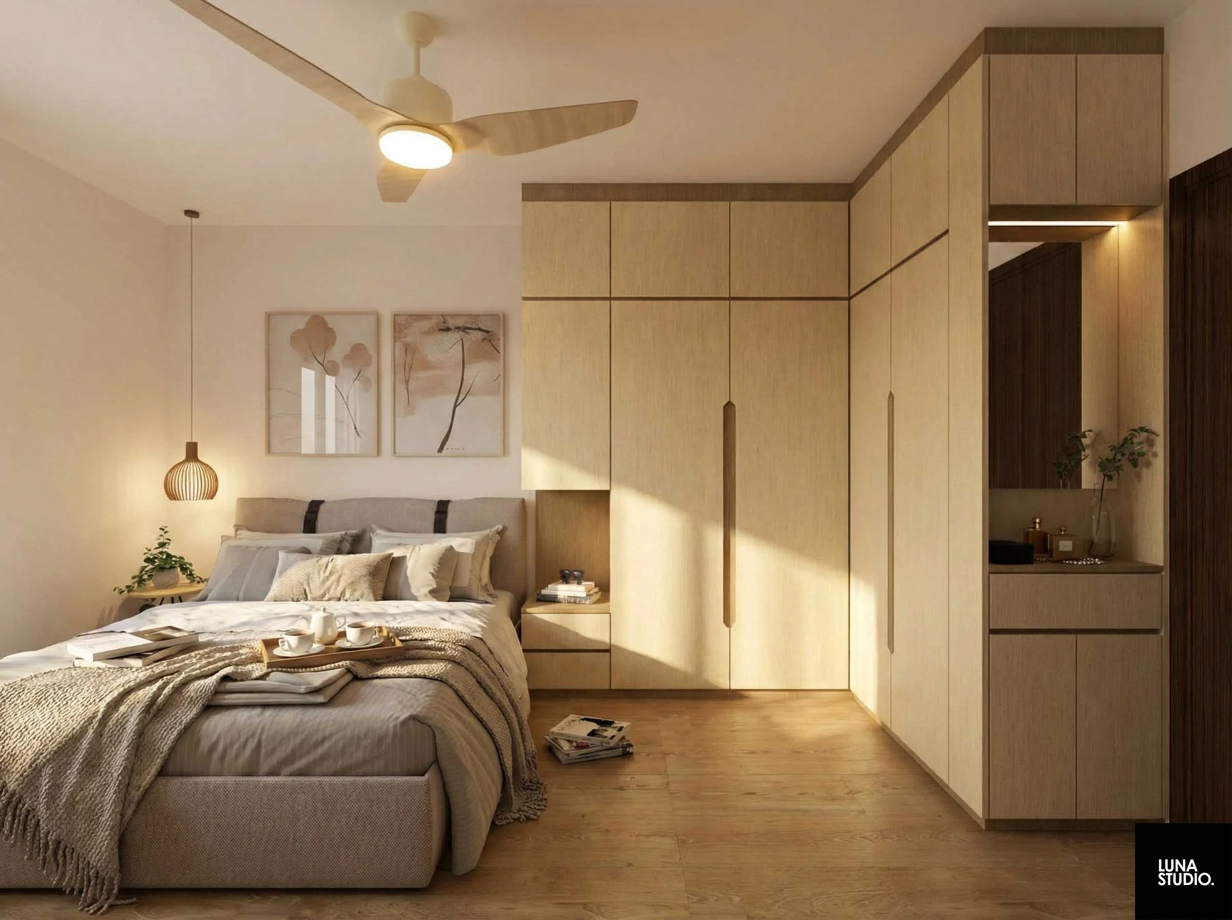 Bedroom with a beige bed, cushions, and a blanket, next to a nightstand with books and a plant. Light-colored wooden wardrobe on the right and two framed minimalist art pieces above the bed. Hanging pendant light and ceiling fan.