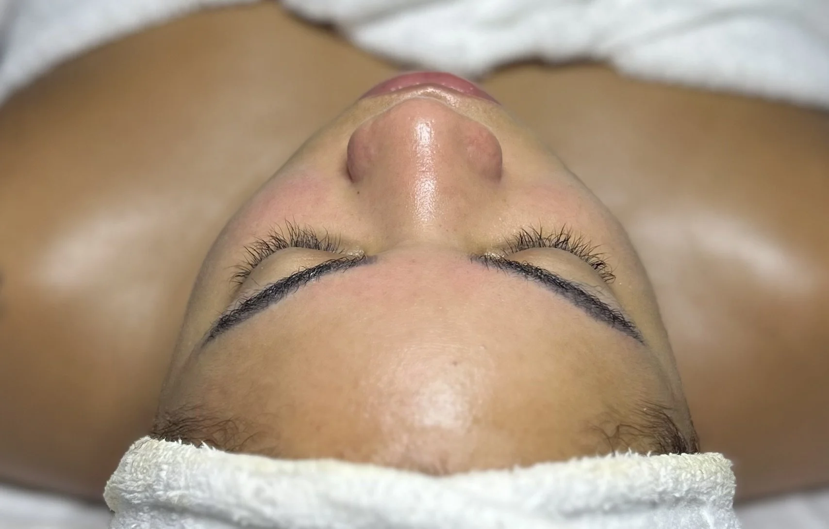Close-up of a woman's face during a facial treatment, lying on a towel with eyes closed.