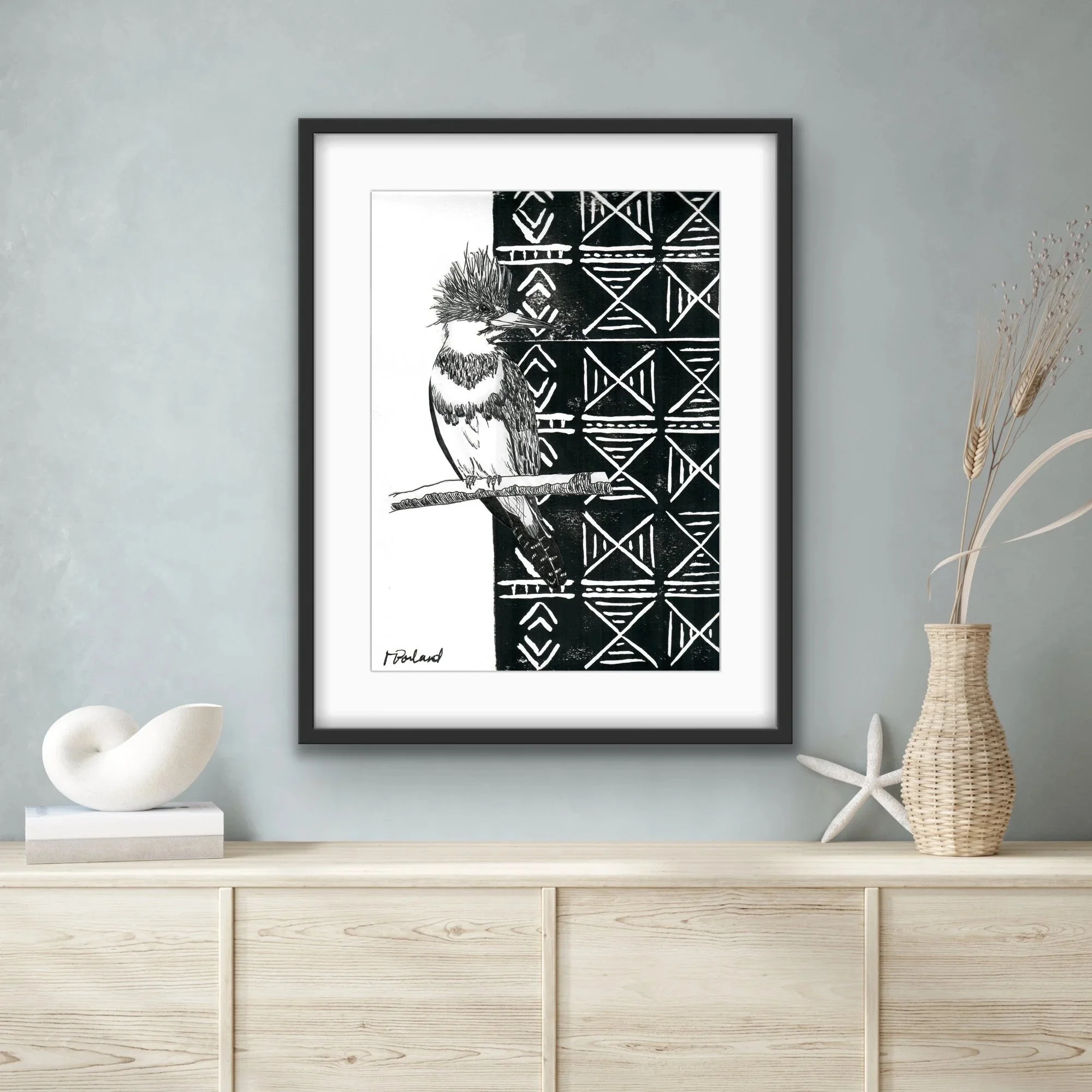 Black and white illustration of a bird perched on a branch against a patterned background, signed 'Podland' at the bottom left, hung on a wall in a modern room.