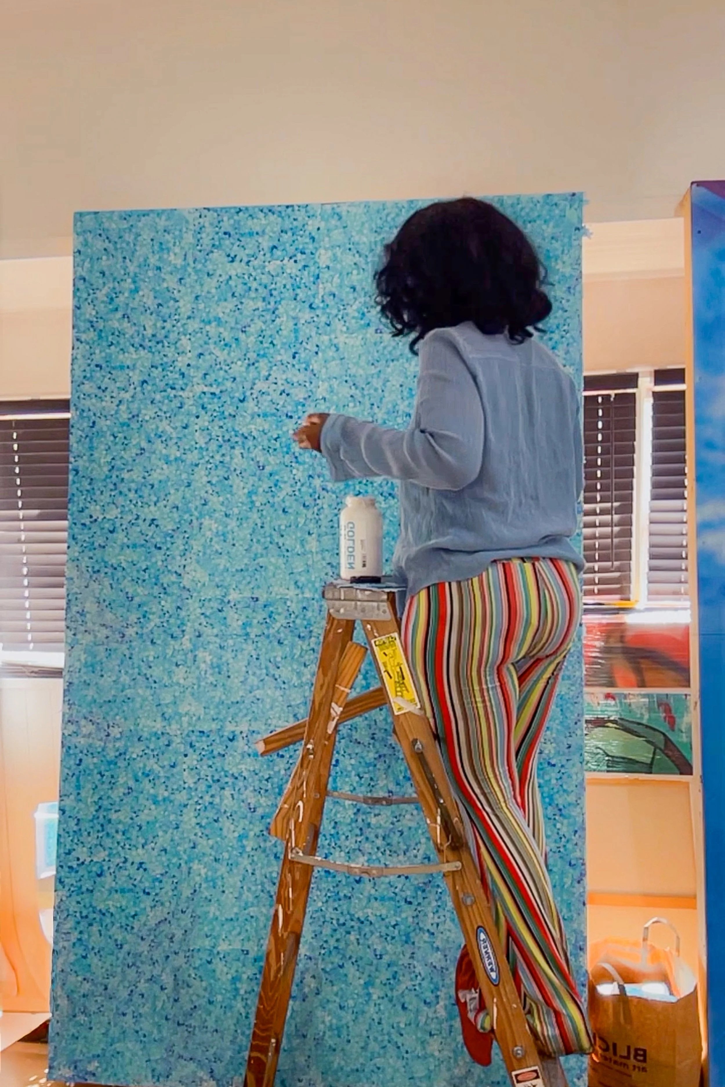 Mixed-media artist Asia Armour creating a large-scale blue artwork in her studio using painting and collage materials.