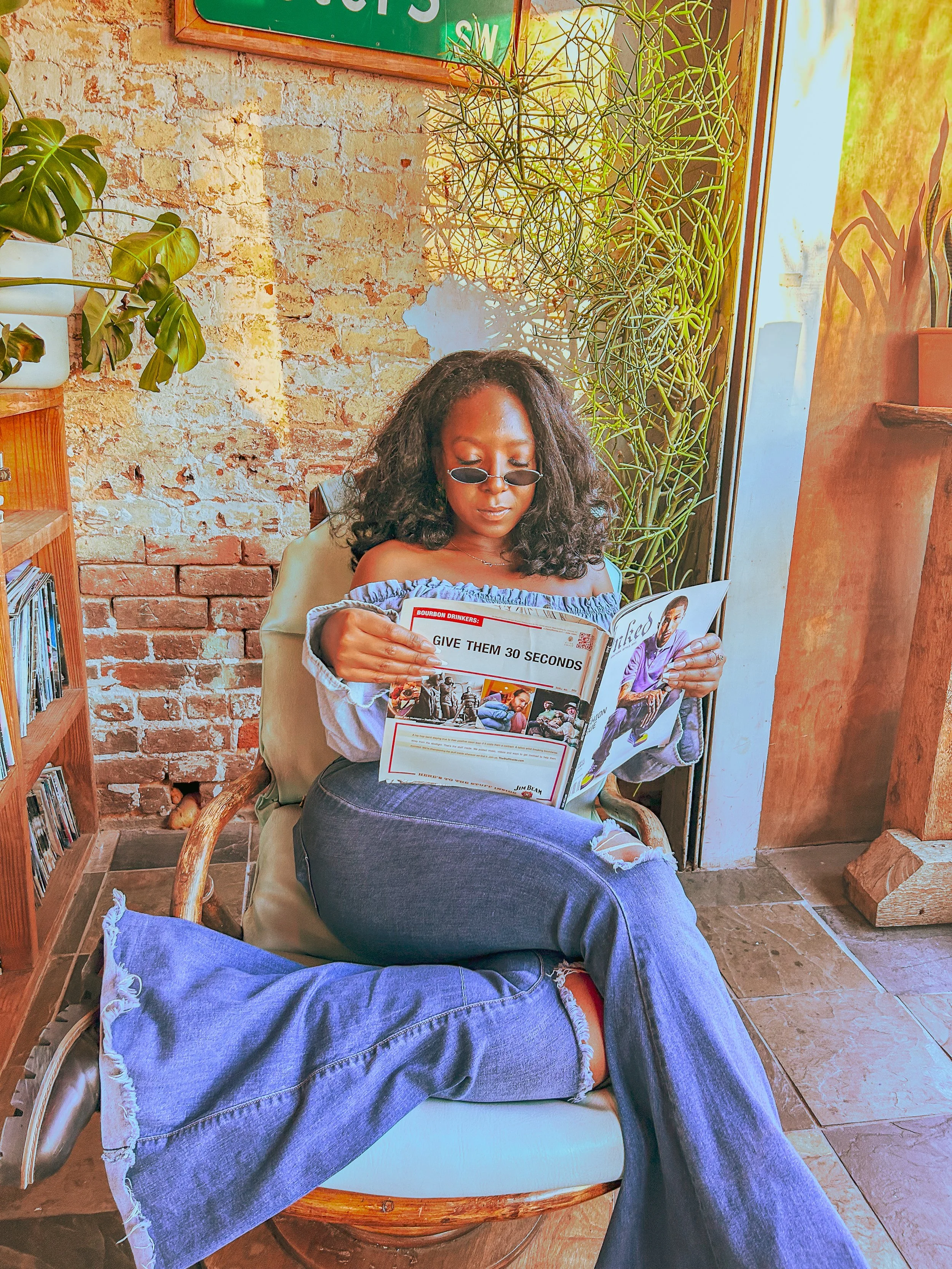 Artist Asia Armour reading a magazine in a plant-filled creative space, reflecting her love of art, fashion and visual storytelling.