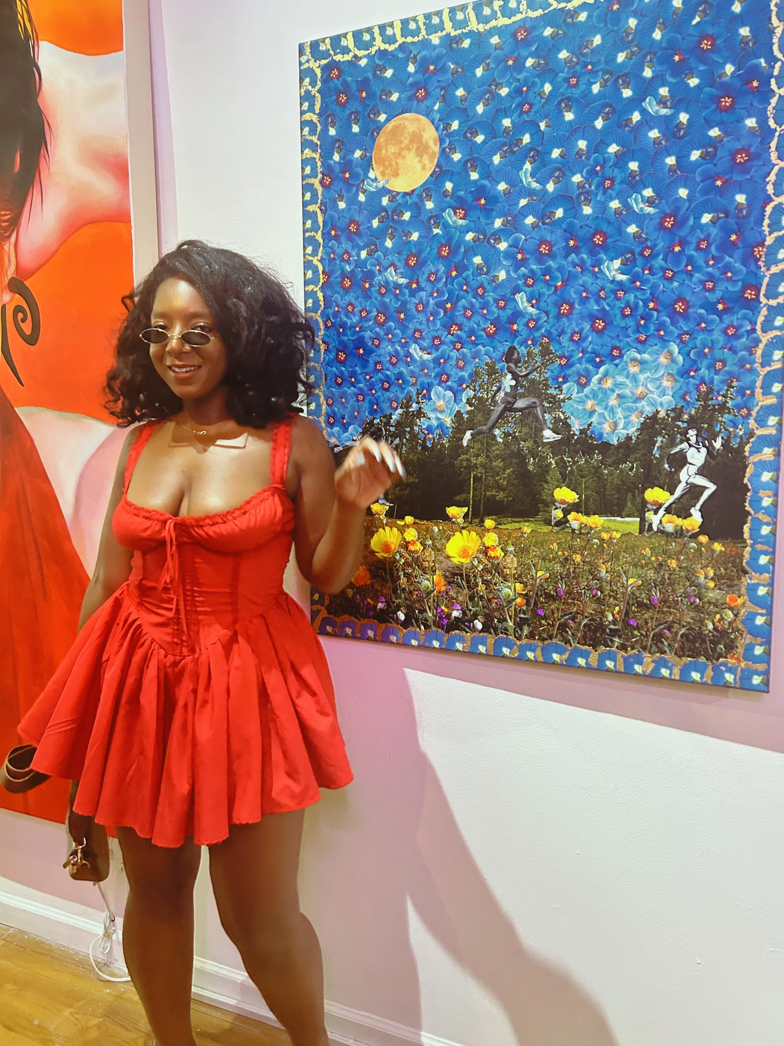 Artist Asia Armour standing beside her colorful mixed-media floral artwork featuring a blue sky, flowers and layered imagery.