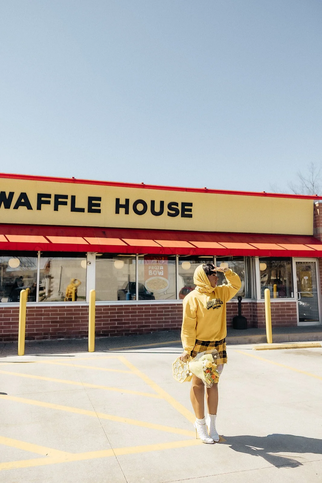 Asia Armour wearing a yellow outfit and holding flowers outside a Waffle House during a lifestyle brand photography shoot.