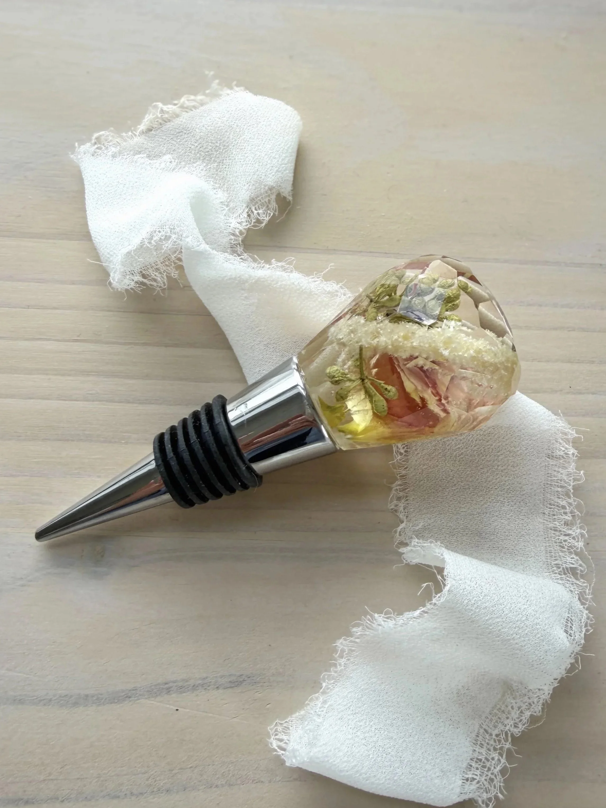 Two decorative hammer-shaped objects with faceted crystal or stone heads and shiny metallic handles, placed on a light-colored surface with a white ribbon and green leaves nearby.