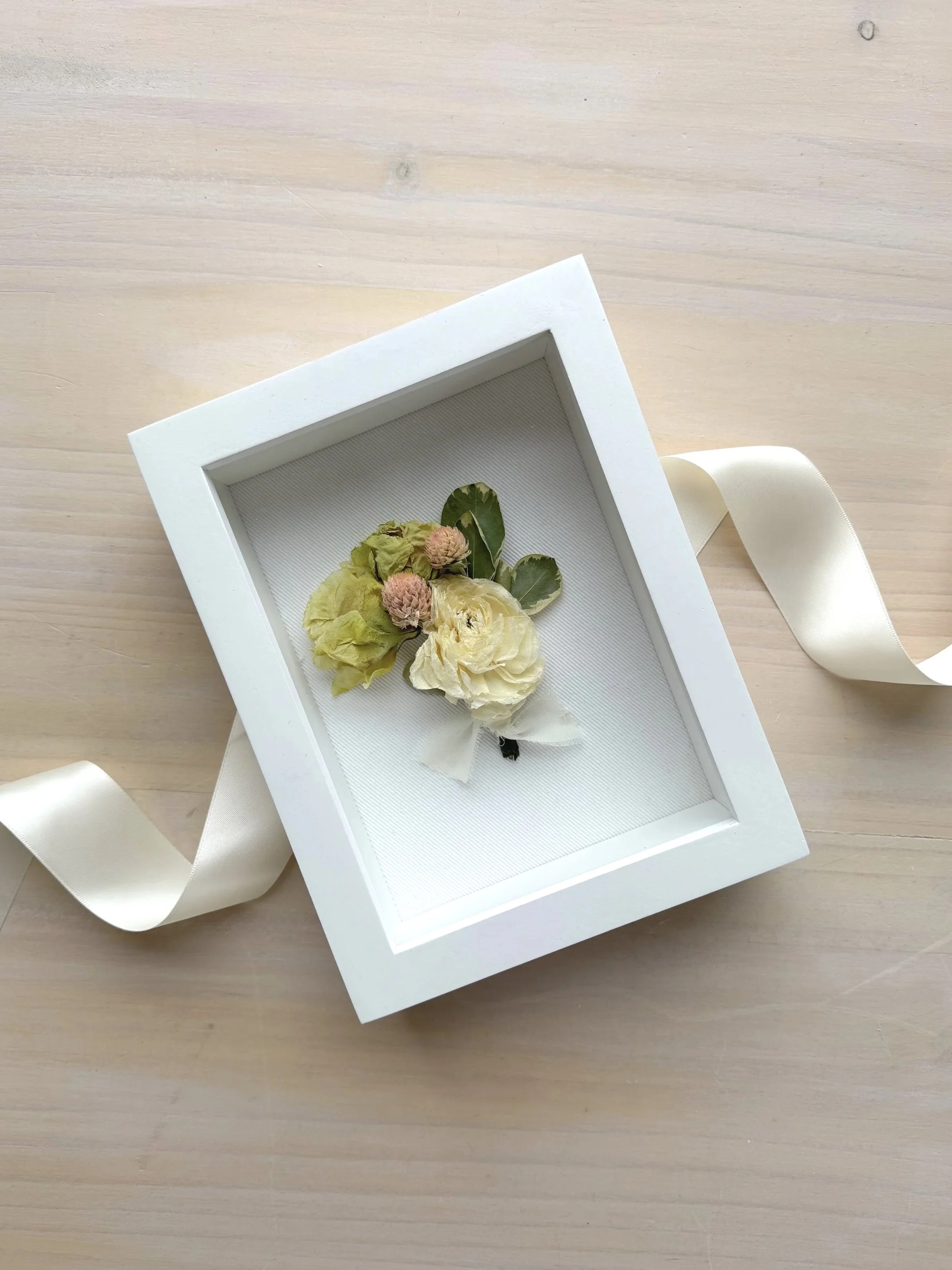 white boutonierre in a white framed shadow box