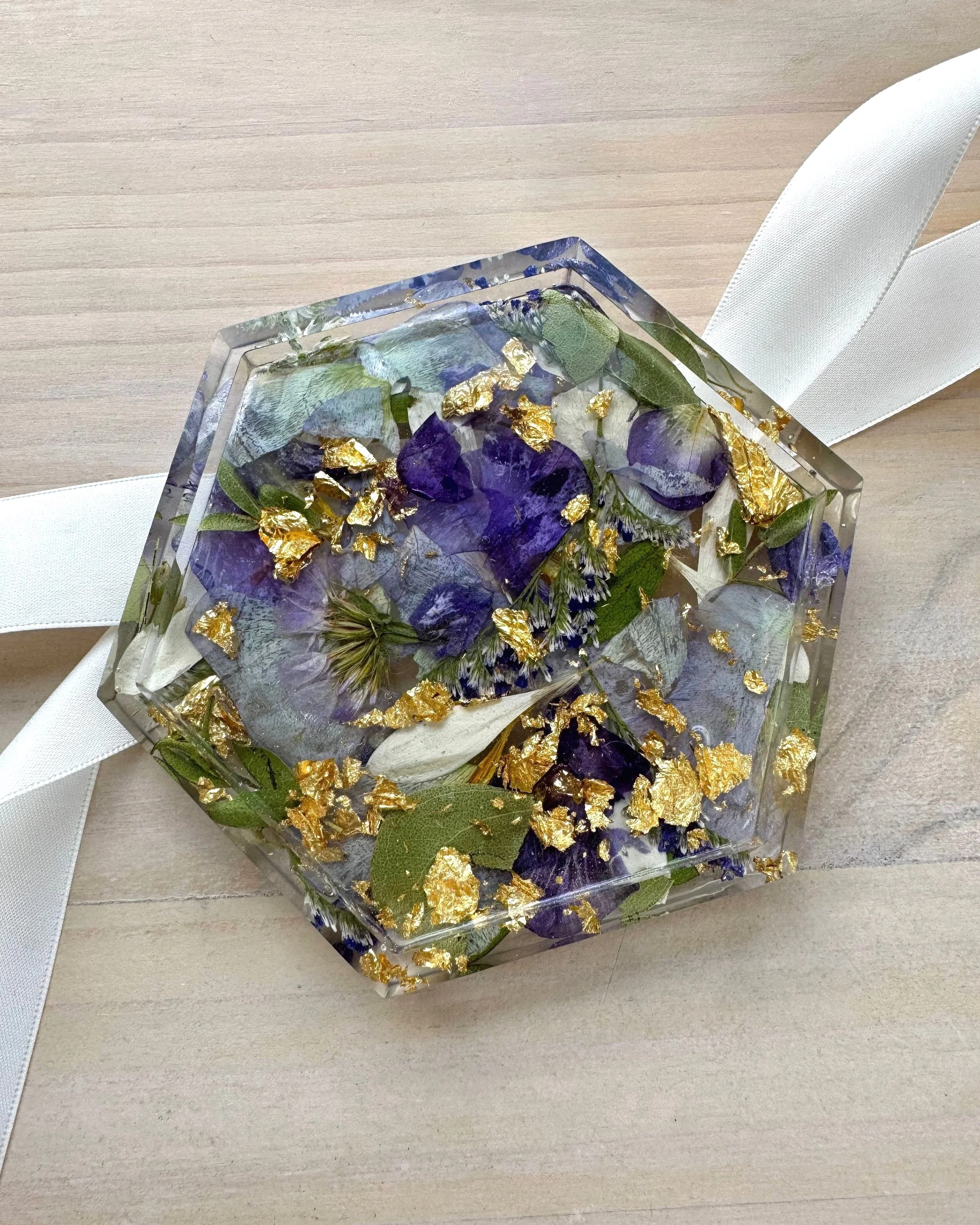 Decorative resin square with pink, purple, orange, and gold flower petals and leaves embedded inside, surrounded by pink and white ribbons and green leaves.
