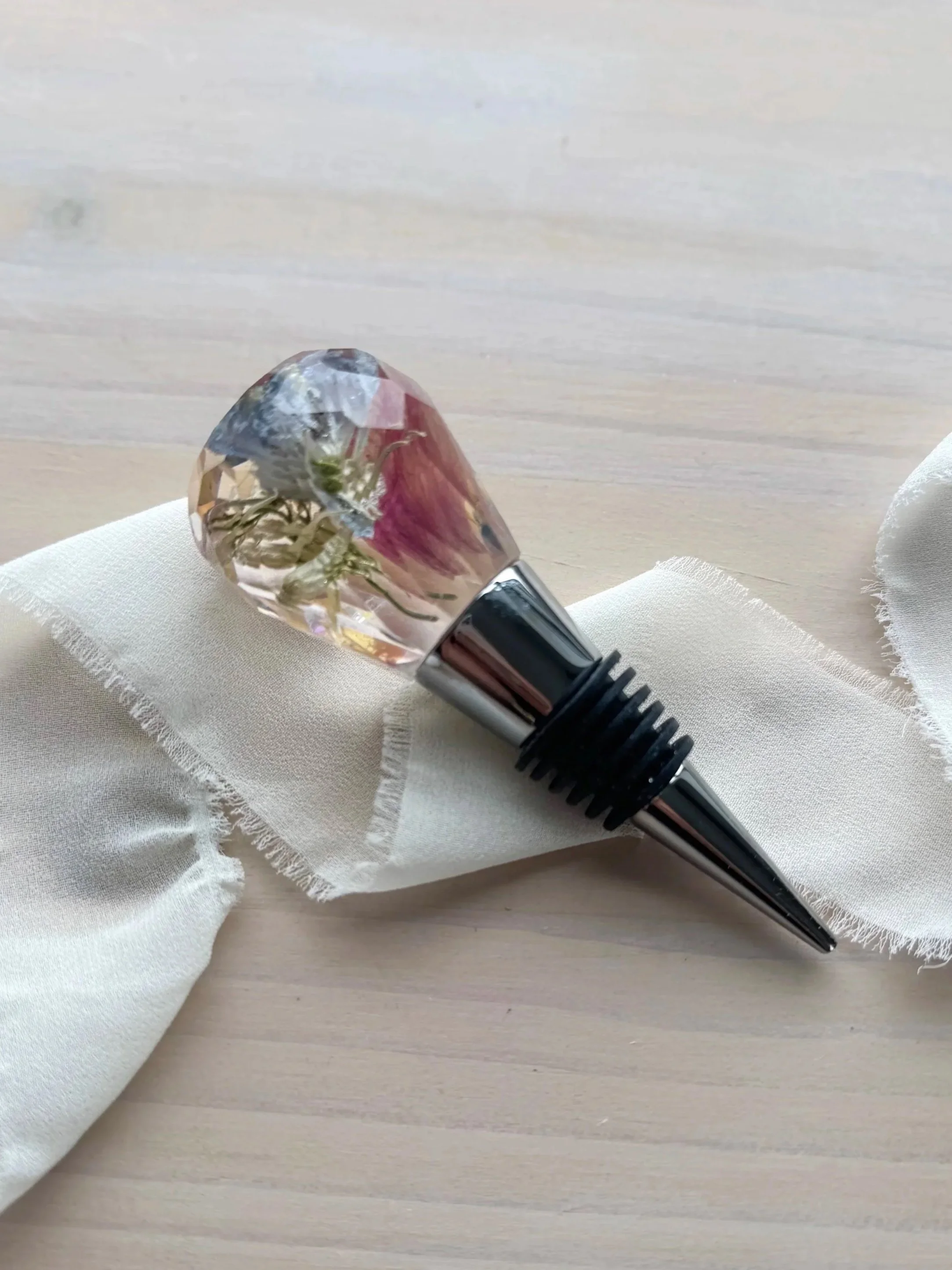 Two decorative hammer-shaped objects with faceted crystal or stone heads and shiny metallic handles, placed on a light-colored surface with a white ribbon and green leaves nearby.