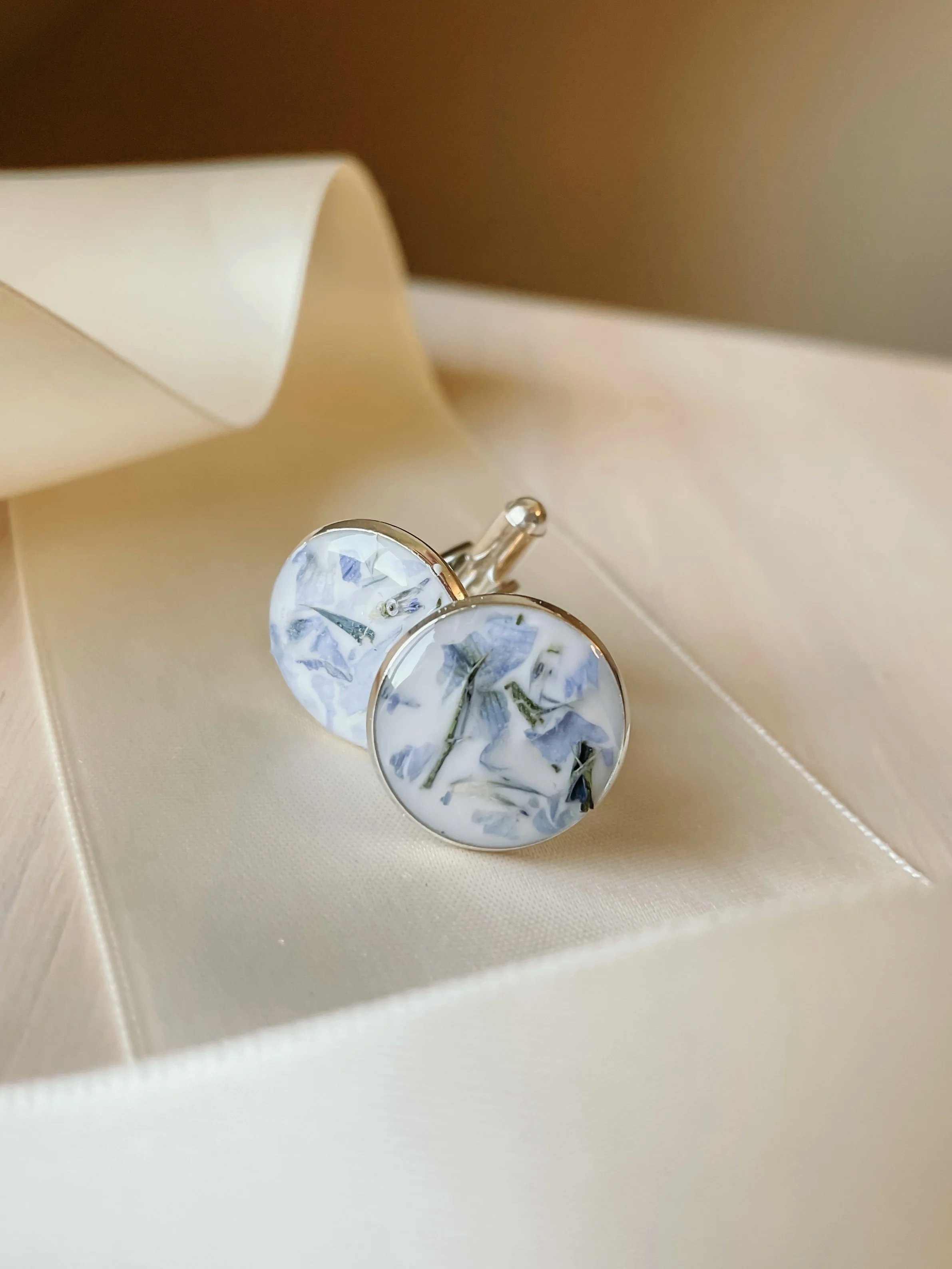 Round marble-patterned cufflinks with blue and white designs, resting on a satin surface inside an open jewelry box.
