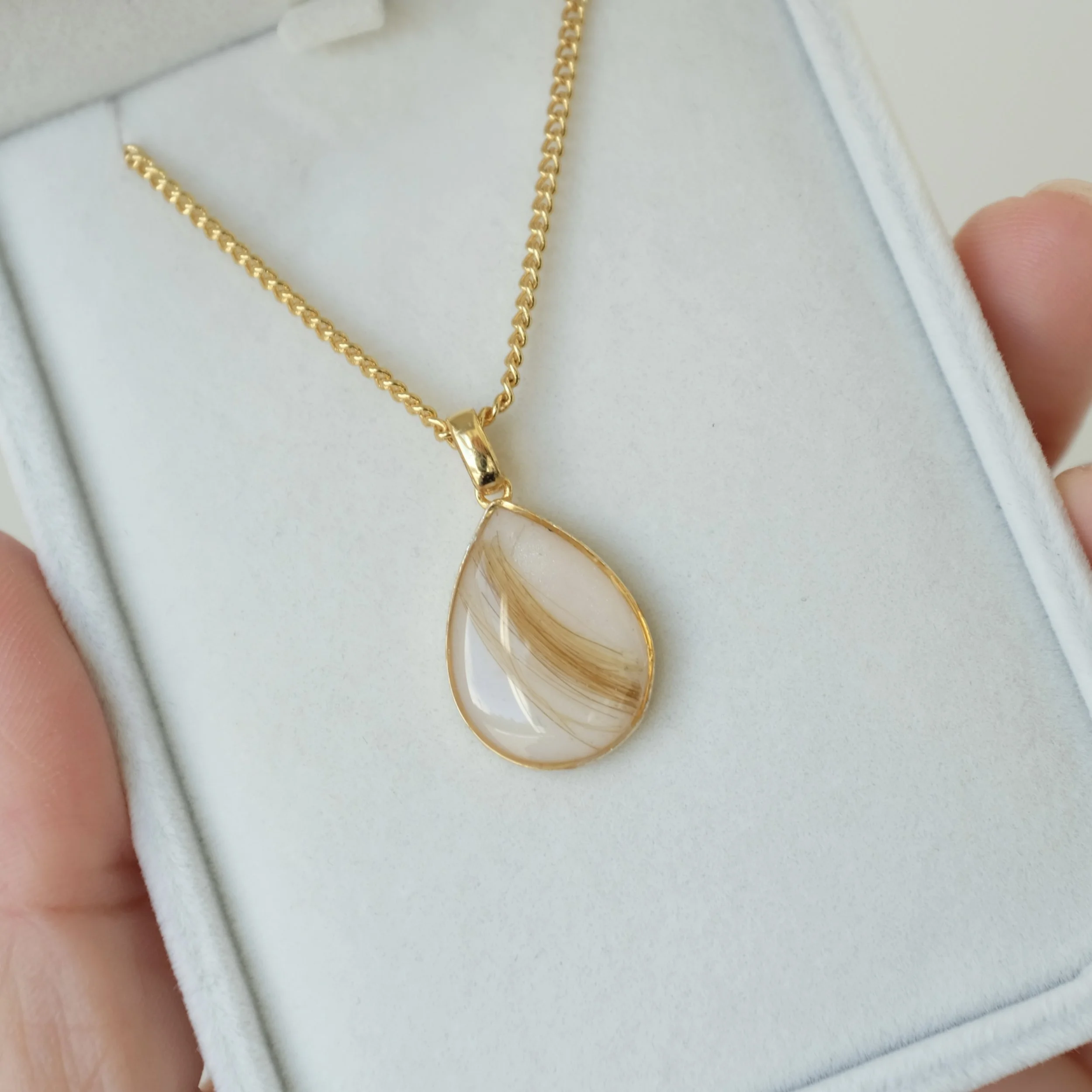 Gold teardrop shaped pendant with resin and a golden lock of hair in the centre