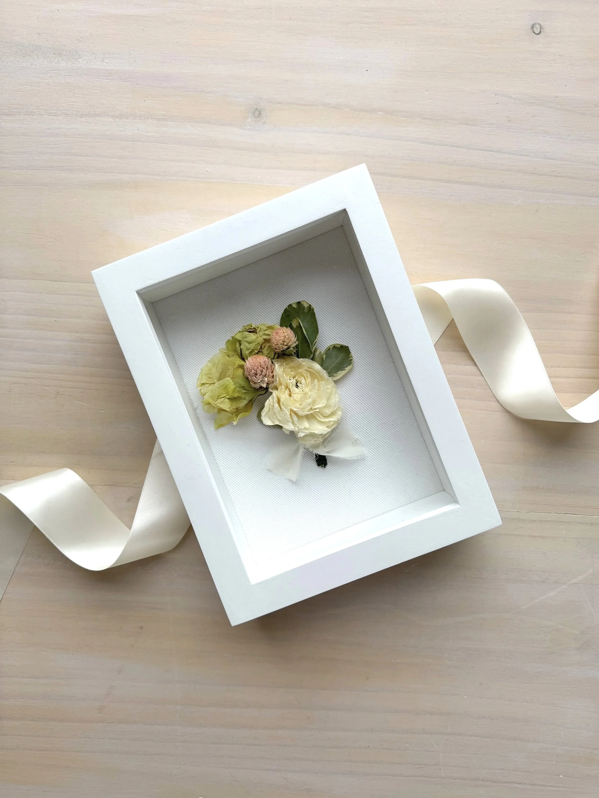 white boutonierre in a white framed shadow box