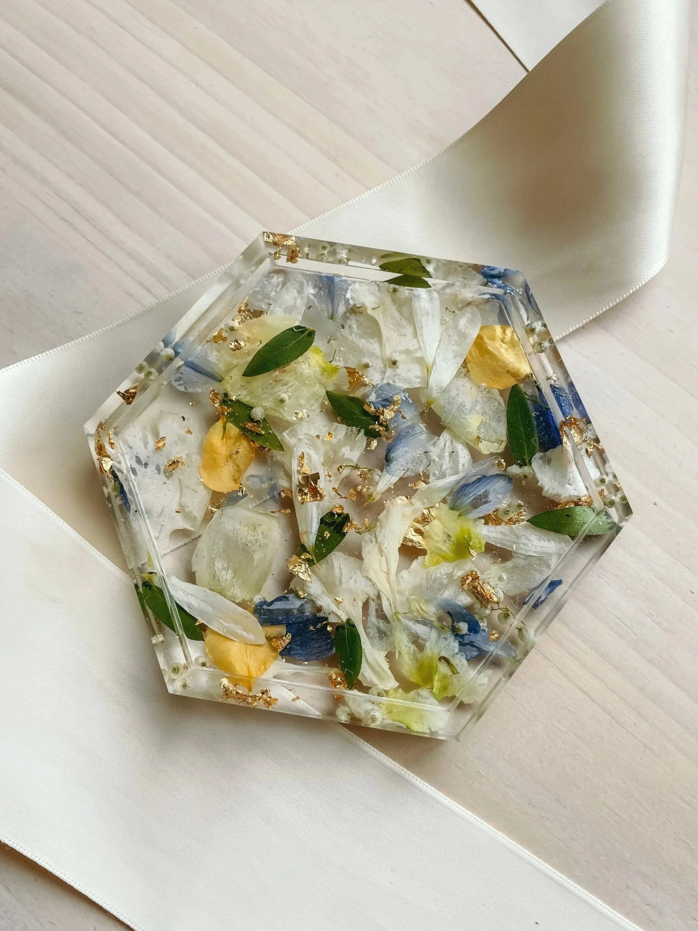 Decorative resin square with pink, purple, orange, and gold flower petals and leaves embedded inside, surrounded by pink and white ribbons and green leaves.