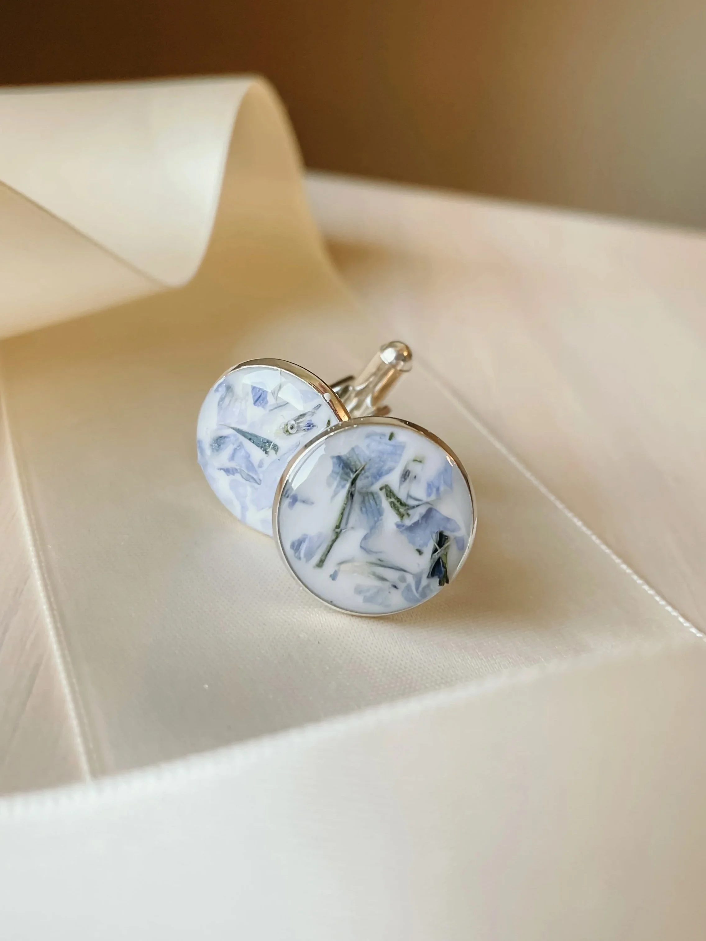 Round marble-patterned cufflinks with blue and white designs, resting on a satin surface inside an open jewelry box.