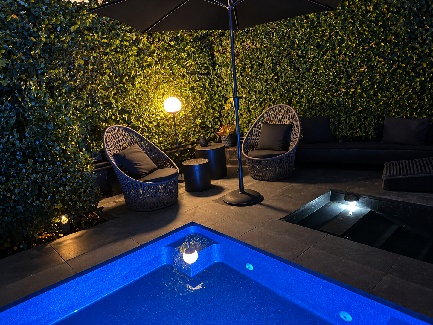 This stunning pool area is a haven of privacy and relaxation. Luxurious woven swivel egg chairs, paired with two circular concrete tables, create an inviting space for unwinding. The gentle glow of the 'Mooon' lamp and understated solar lighting adds