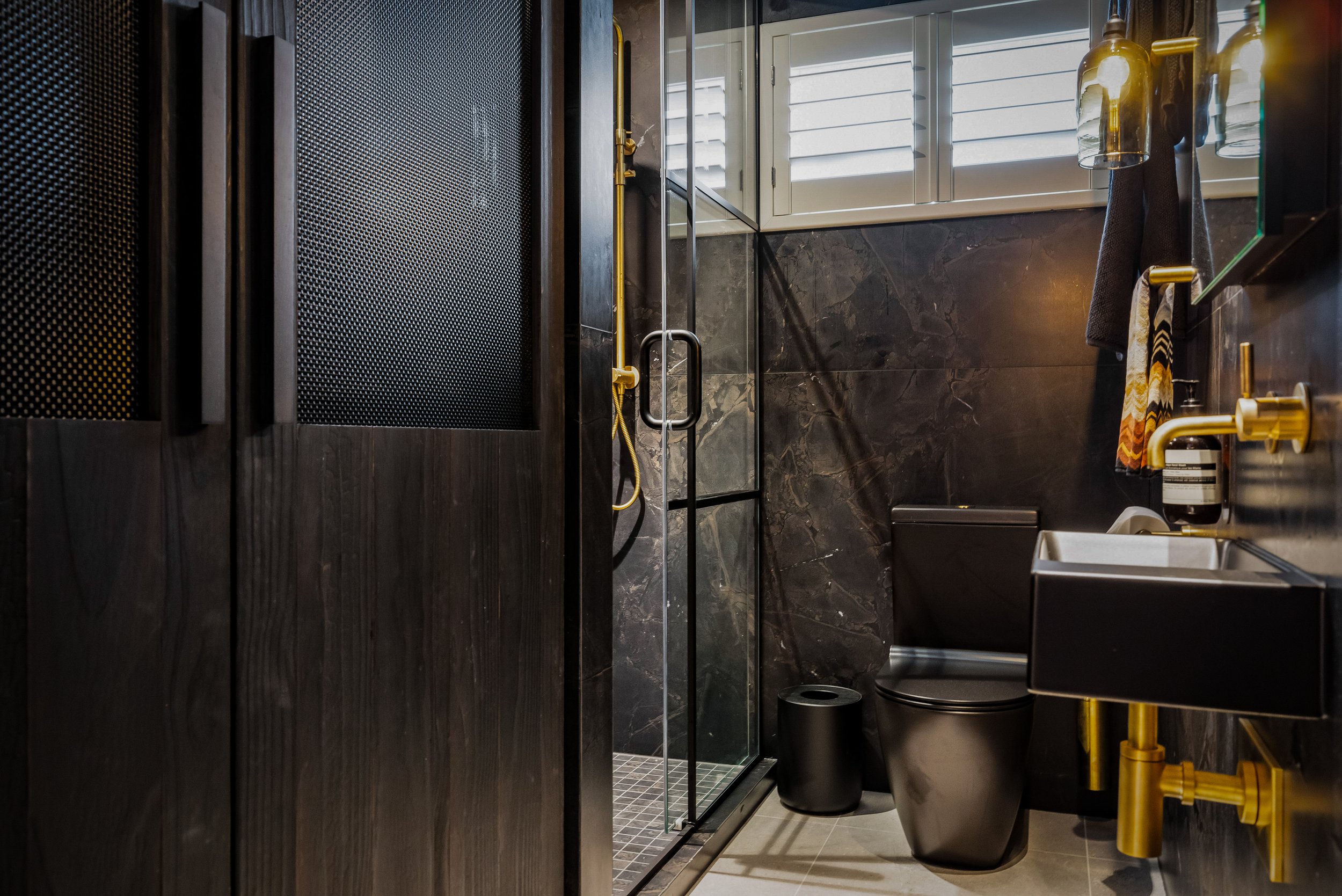 The sensored Monmouth amber pendant beautifully complements the accented aged Progetto tapware, Brazilian tiles, and custom-built concealed laundry, all finished with black toilet and vanity basin.