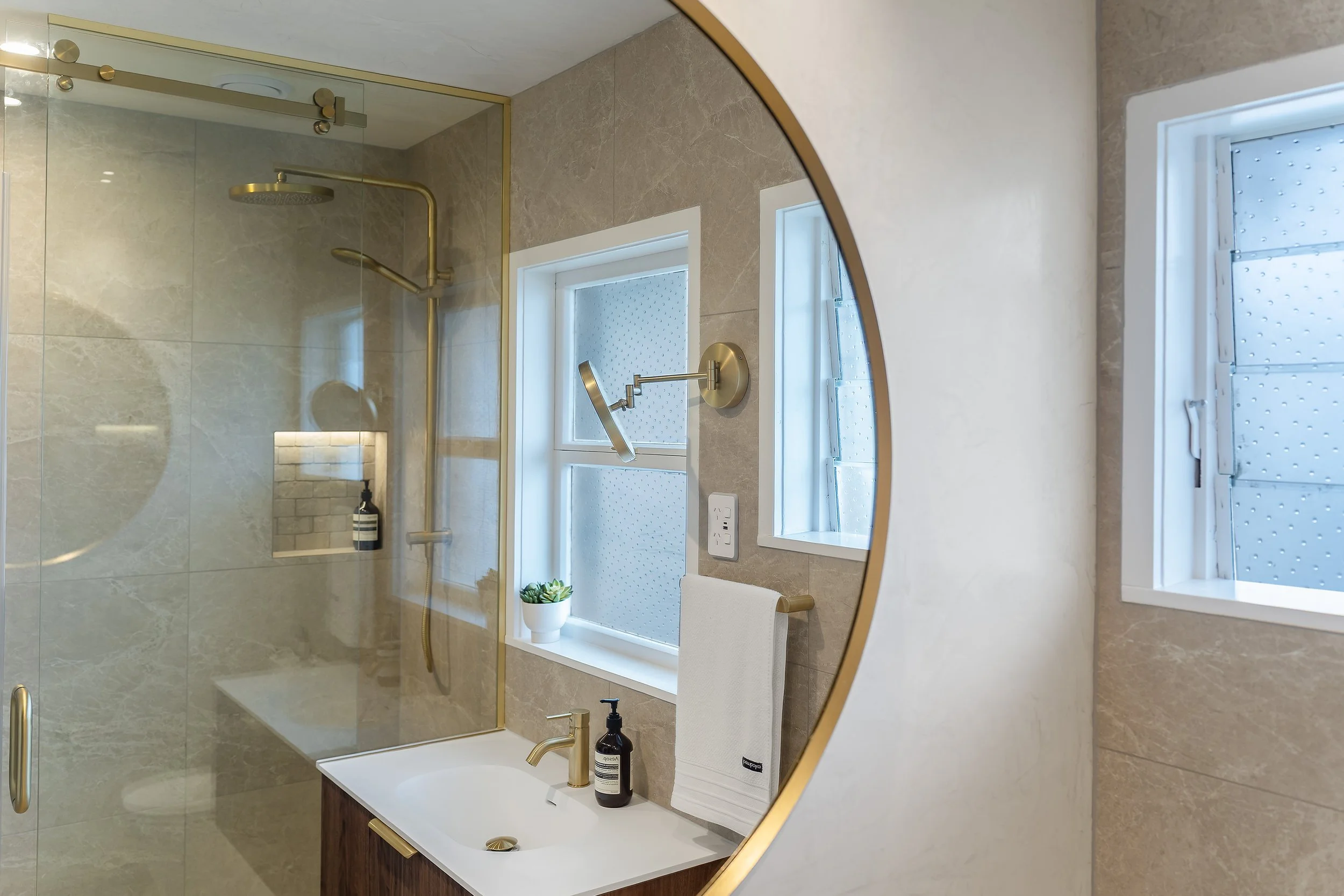 The circular brushed brass mirror is a design trick that instantly expands this compact space. Paired with the custom "fresco" waxed walls—which are as durable as they are stunning—the room feels luxurious and open. Every detail, from the shaving mir