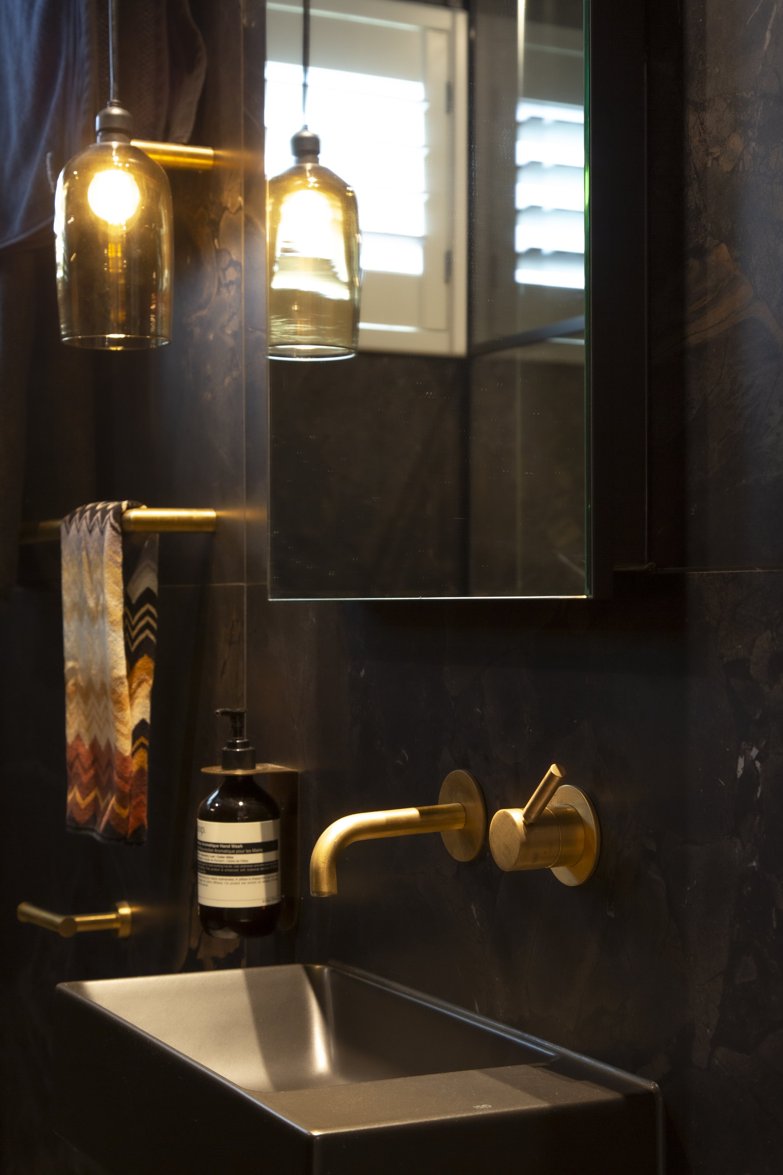 The sensored Monmouth amber pendant beautifully complements the accented aged brass Progetto tapware, Brazilian tiles, and black vanity basin.