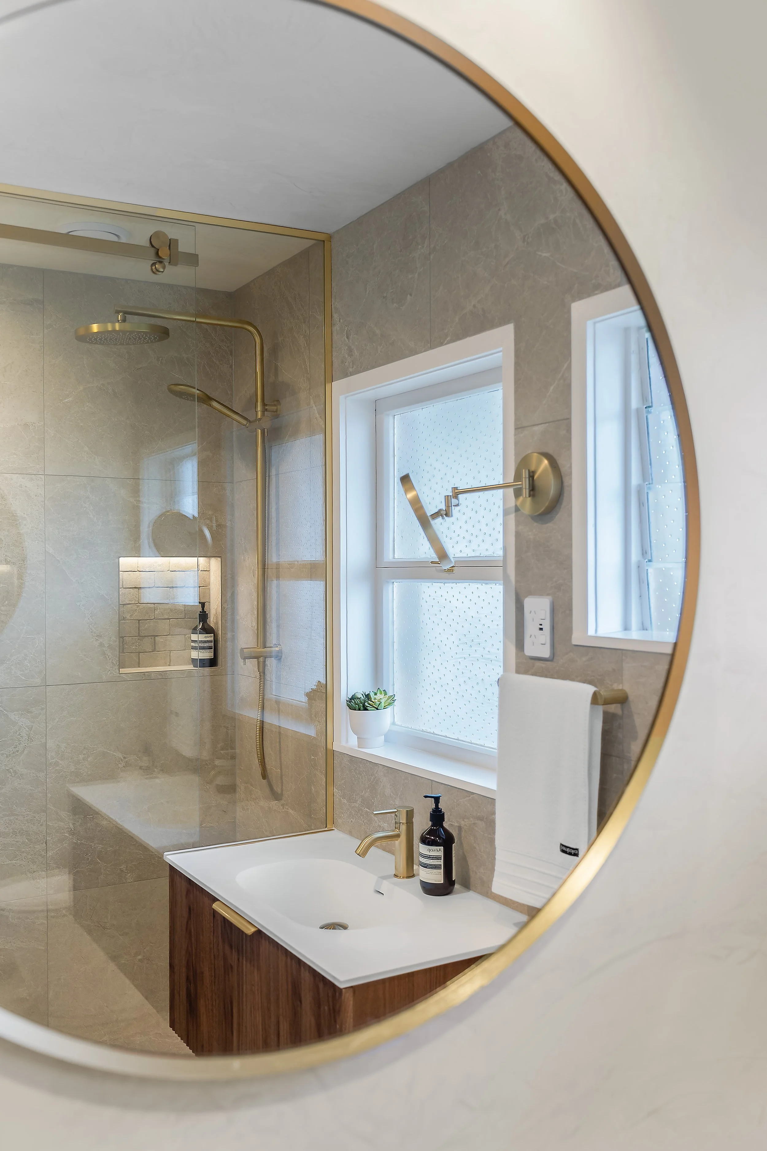 The circular brushed brass mirror is a design trick that instantly expands this compact space. Paired with the custom "fresco" waxed walls—which are as durable as they are stunning—the room feels luxurious and open. Every detail, from the shaving mir