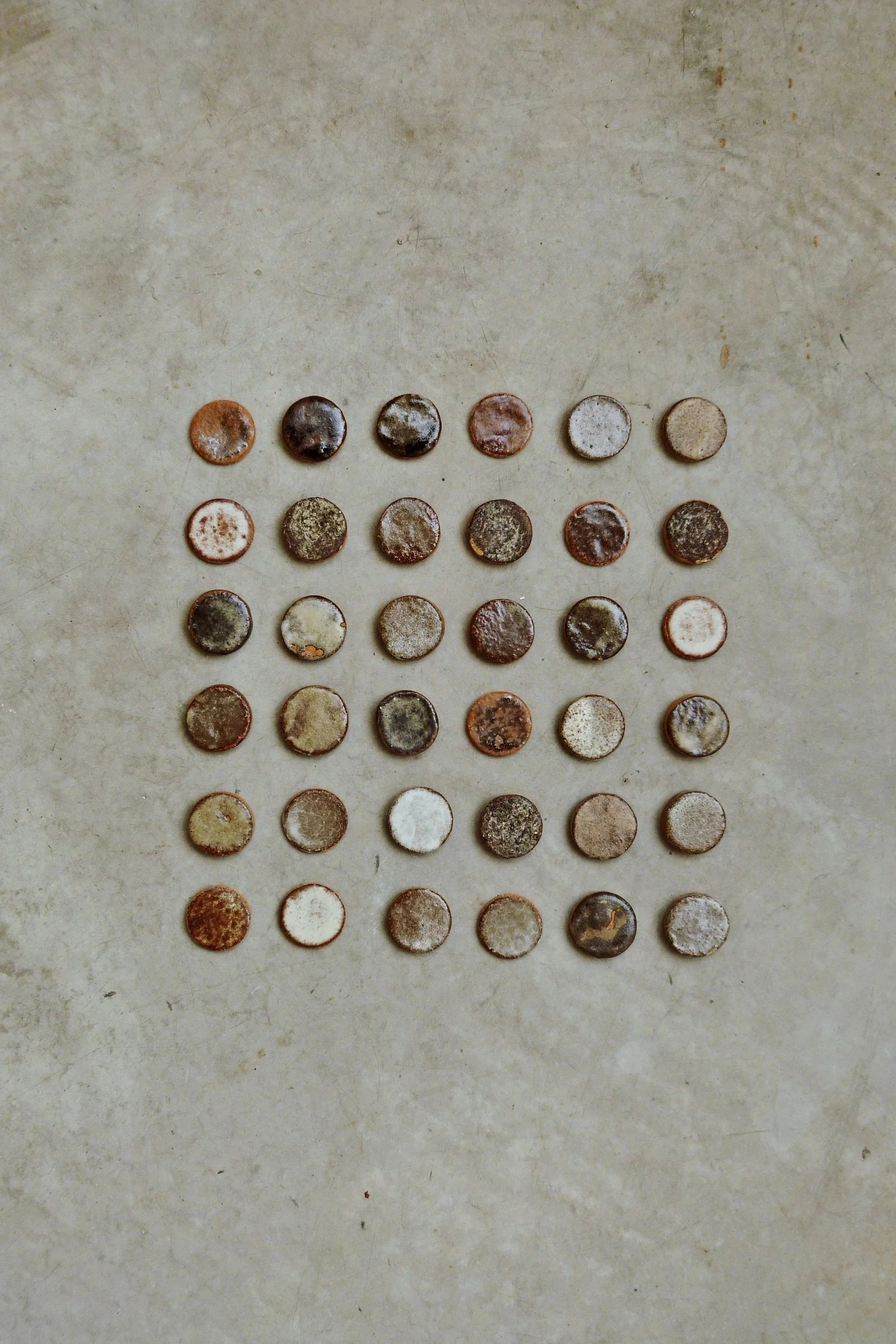 A collection of 30 old, rusty coins arranged in a 6x5 grid on a concrete surface.