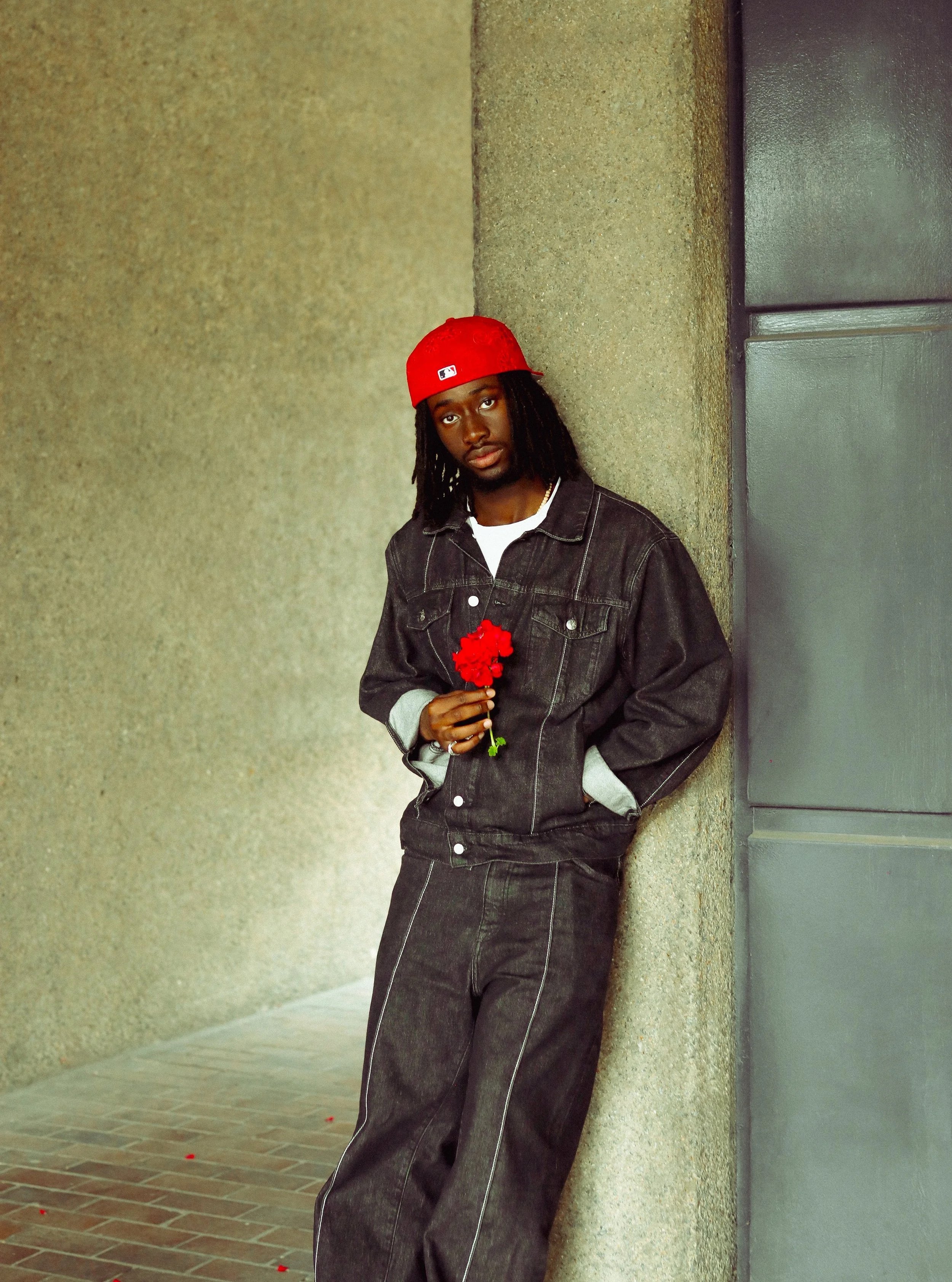 a poet standing with a red flower in his hand. An emotive portrait showing expression and male vulnerability with vibrant red and blue. 