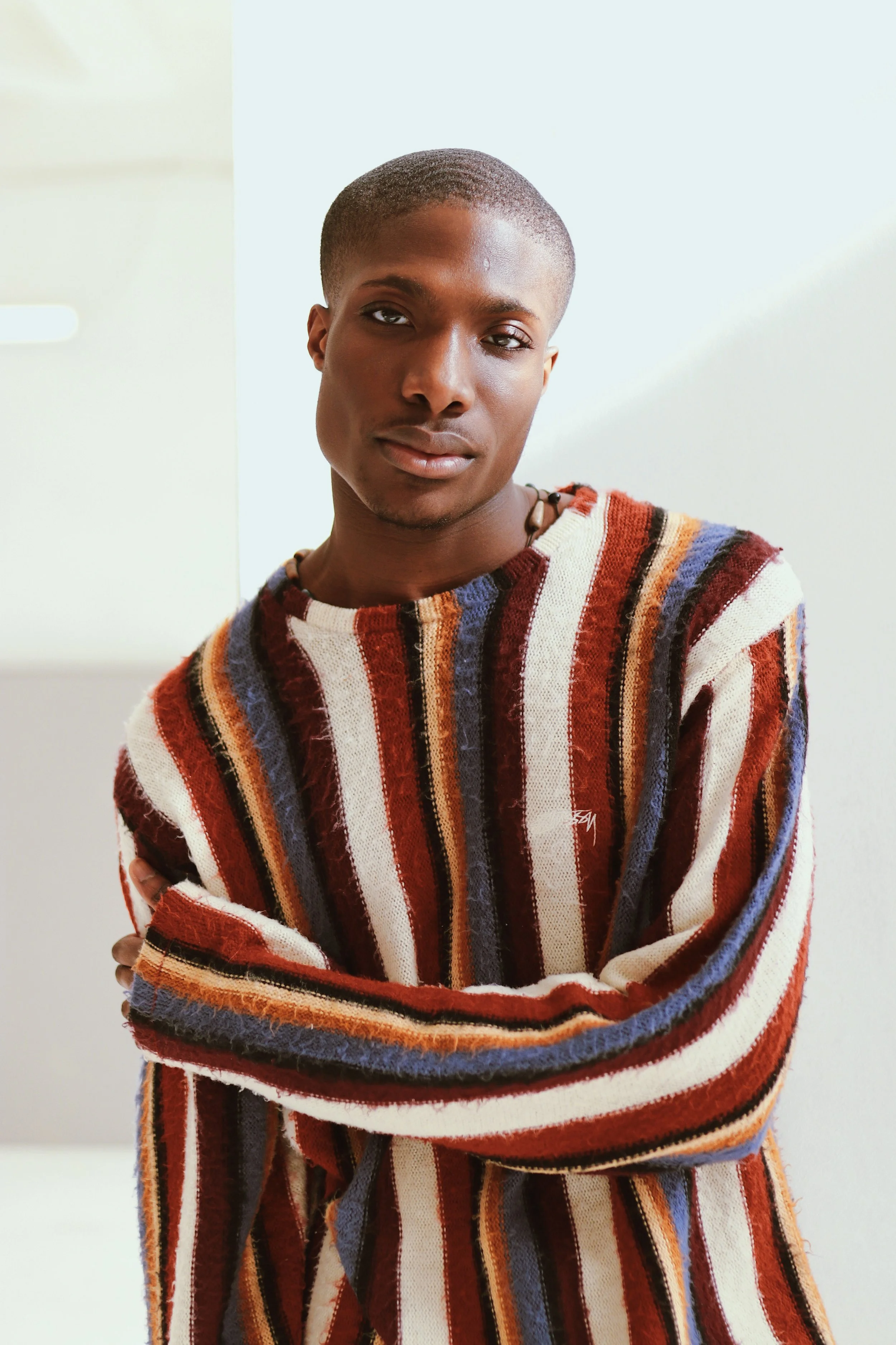 an emotive portrait of a young black man with a subtle smile. With a beautiful natural light creeping from the window above onto his left eye. Rich tones and mood 