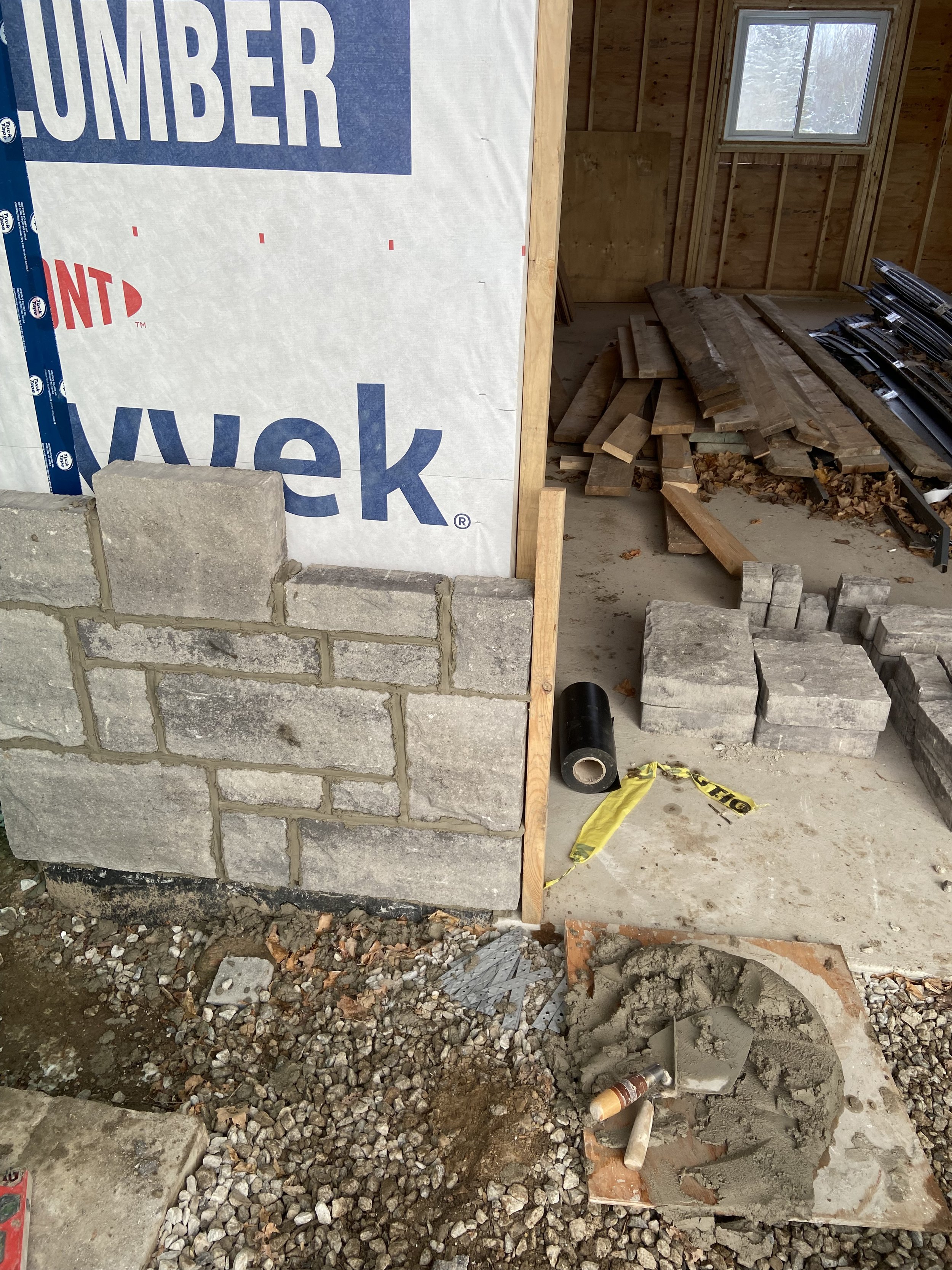 Partially constructed wall with stone bricks and Tyvek wrap, construction materials inside a building under construction.