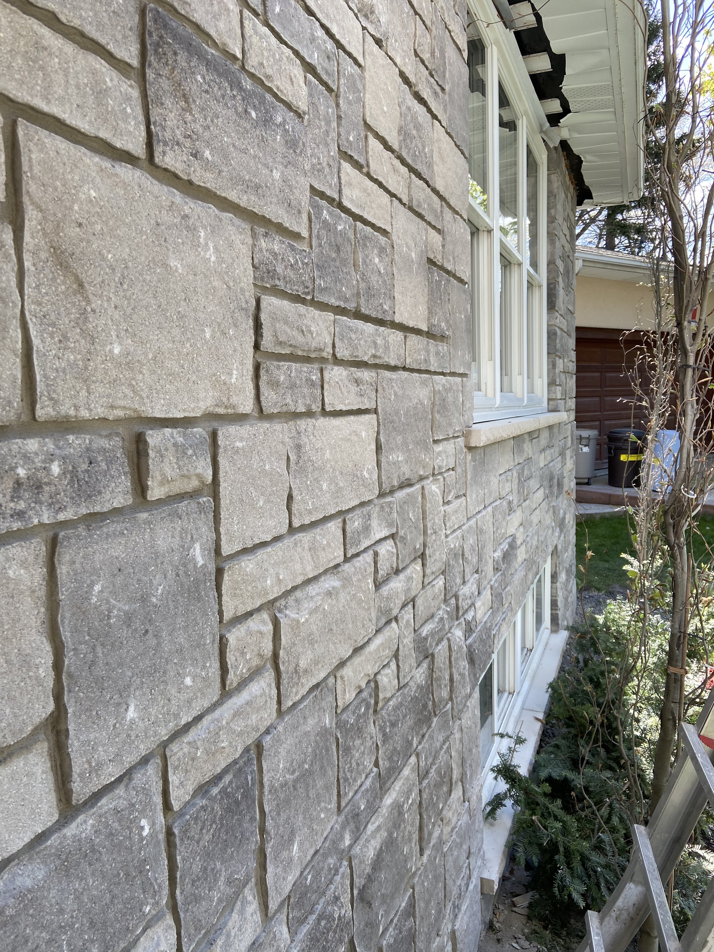 Stone exterior wall of a house with windows and adjacent garden
