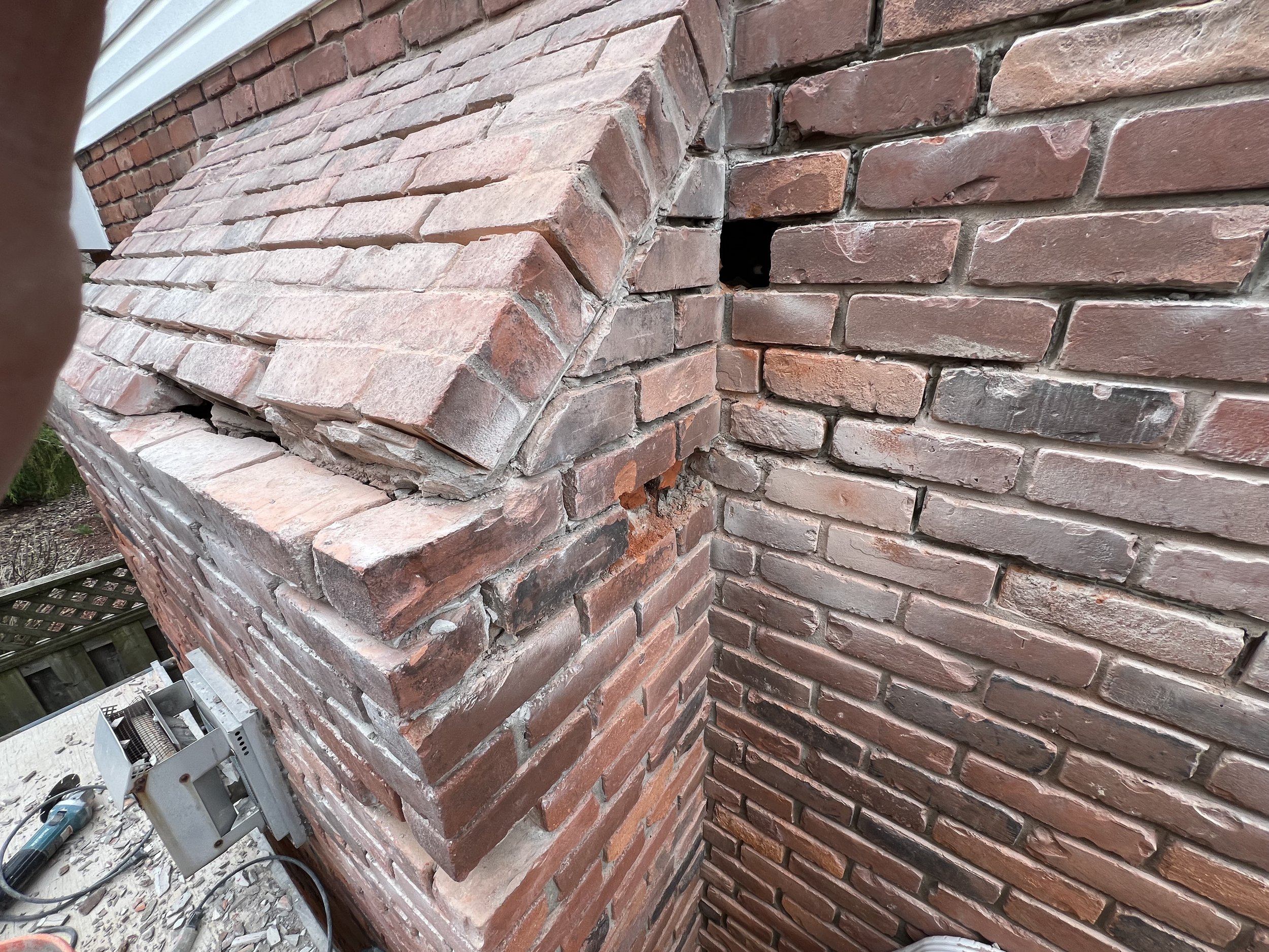 Close-up of damaged brick chimney with dislodged bricks and gaps.