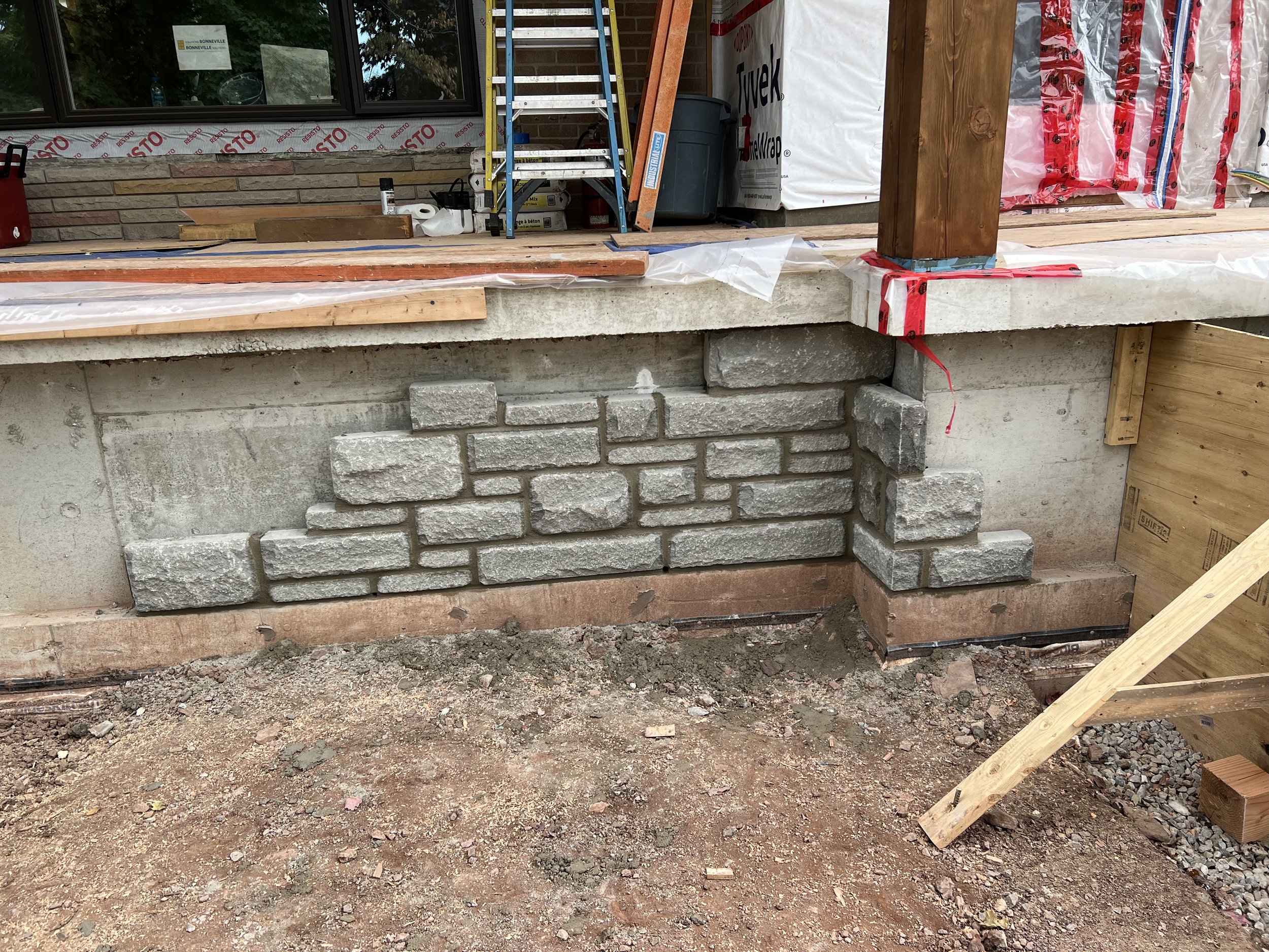 Partially constructed stone veneer on a concrete foundation, with building materials and scaffolding visible.