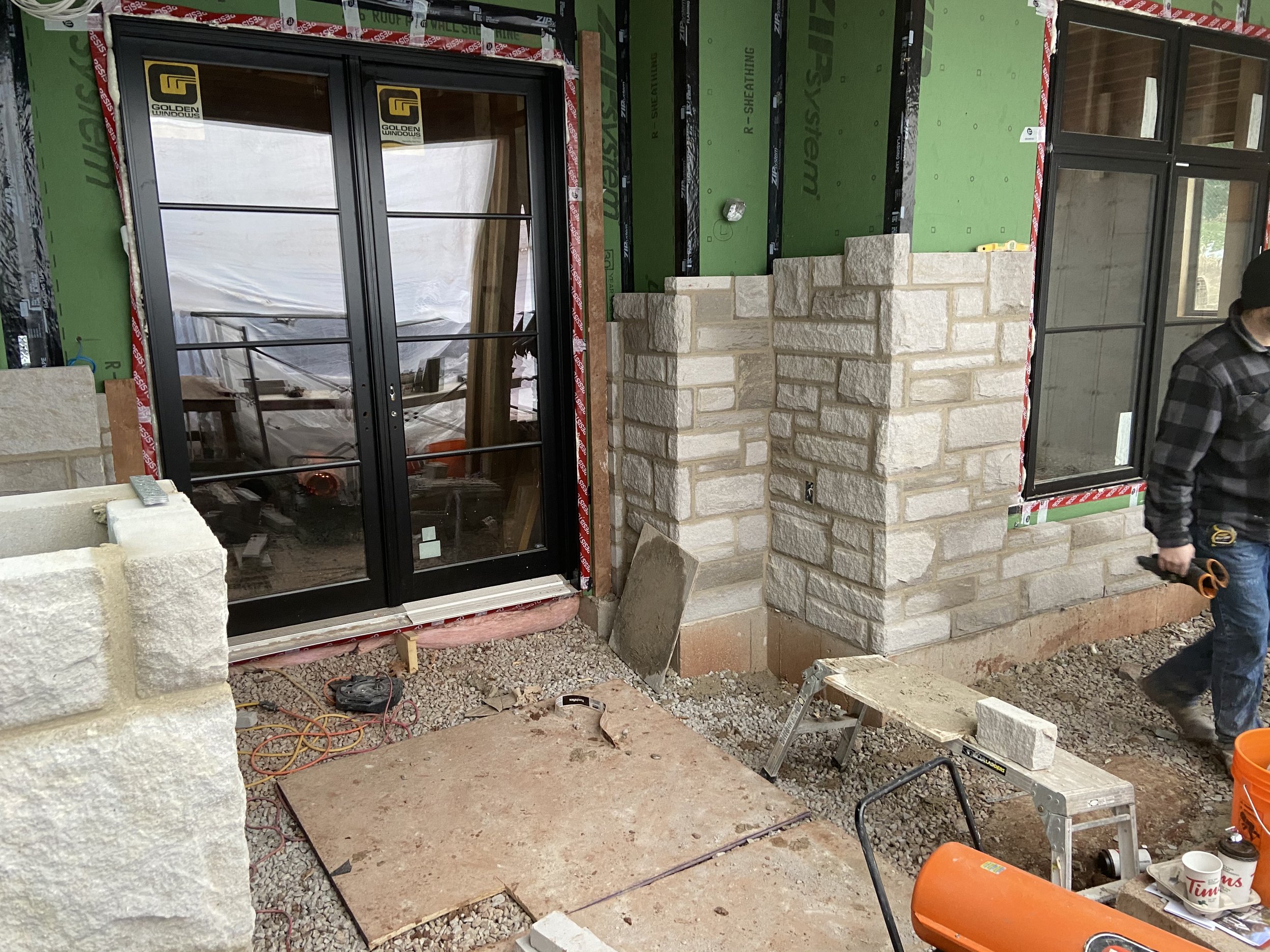 Construction site with stone facade installation, glass doors, tools, and building materials
