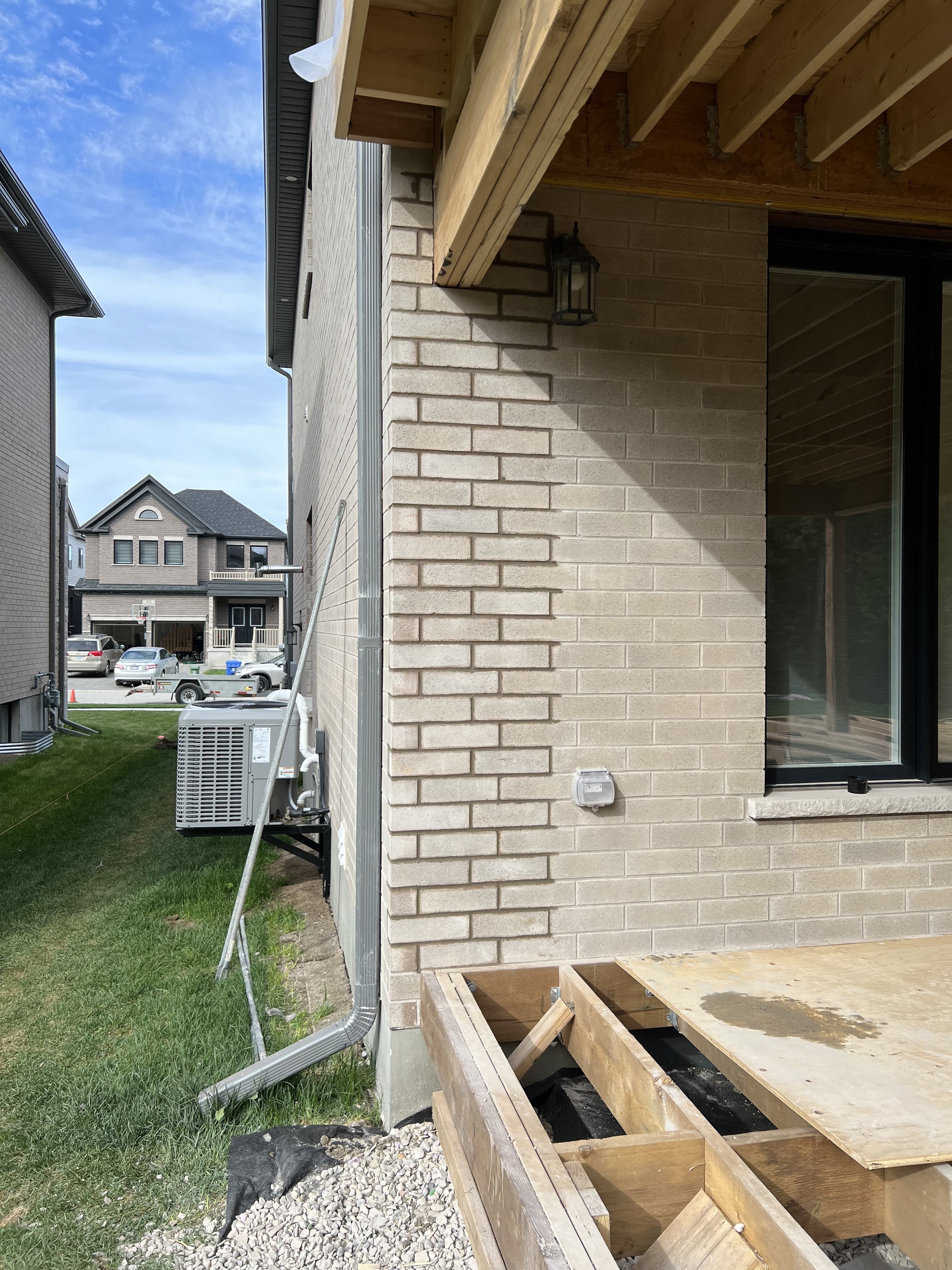 Side of a house with a partial view of a backyard deck under construction, an air conditioning unit, and neighboring houses in the background.