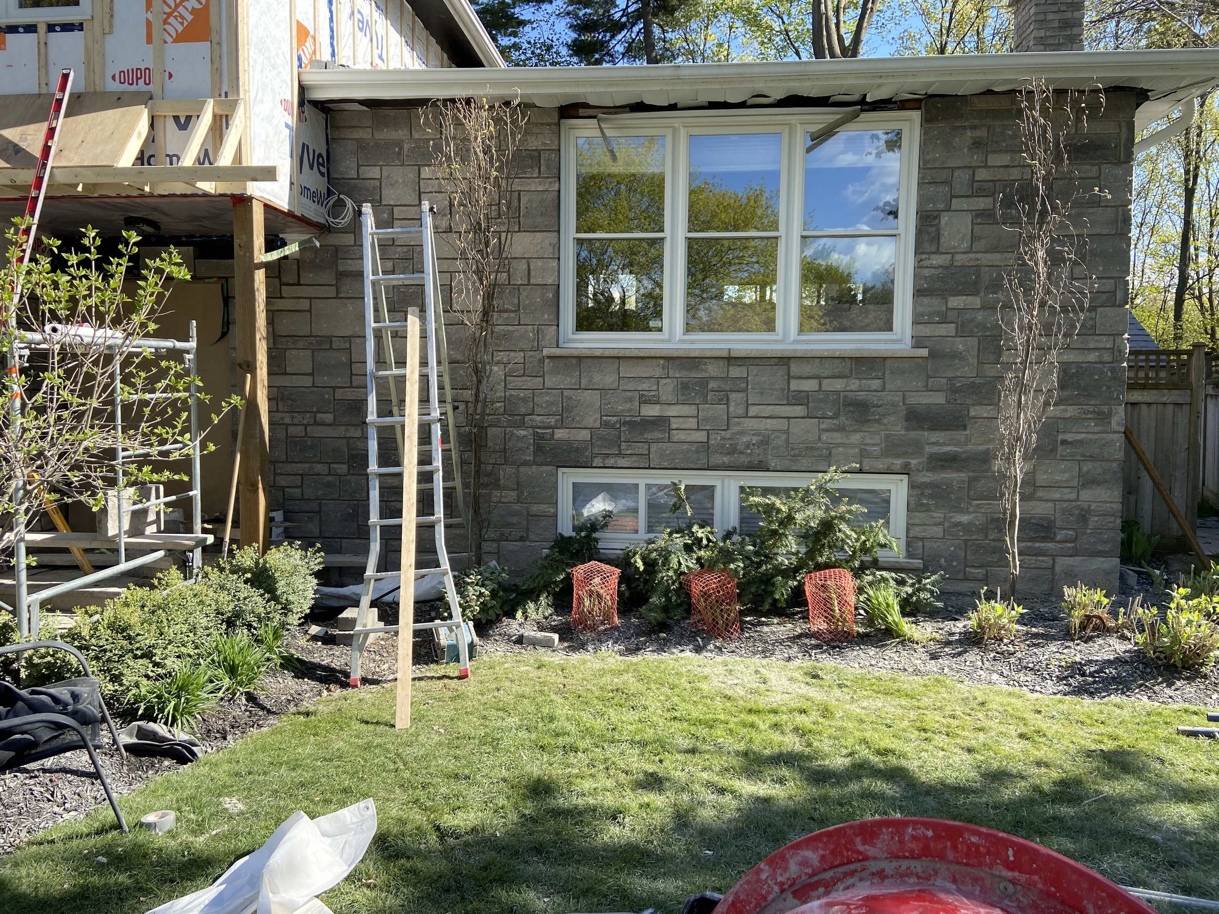 Renovation scene with a brick house, ladders, scaffolding, and construction materials in a garden.