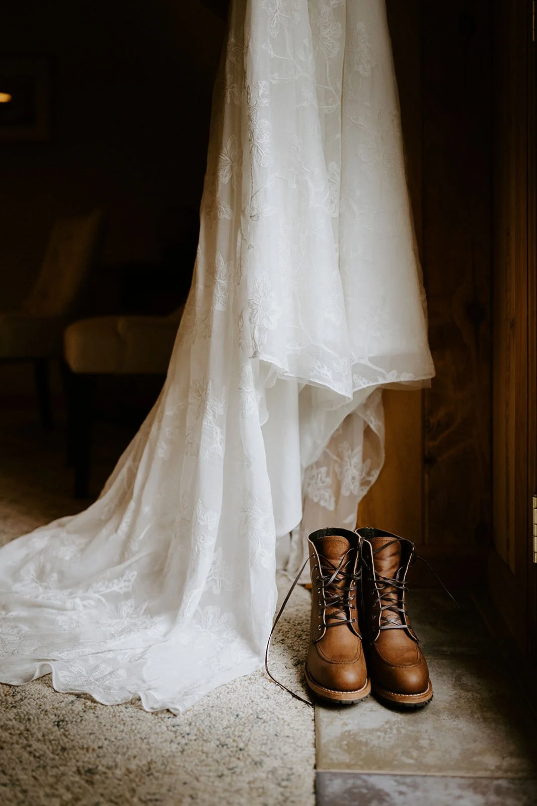 Lace wedding dress hanging in a cabin with a pair of brown Red Wing Iron Ranger leather boots on the floor beneath it