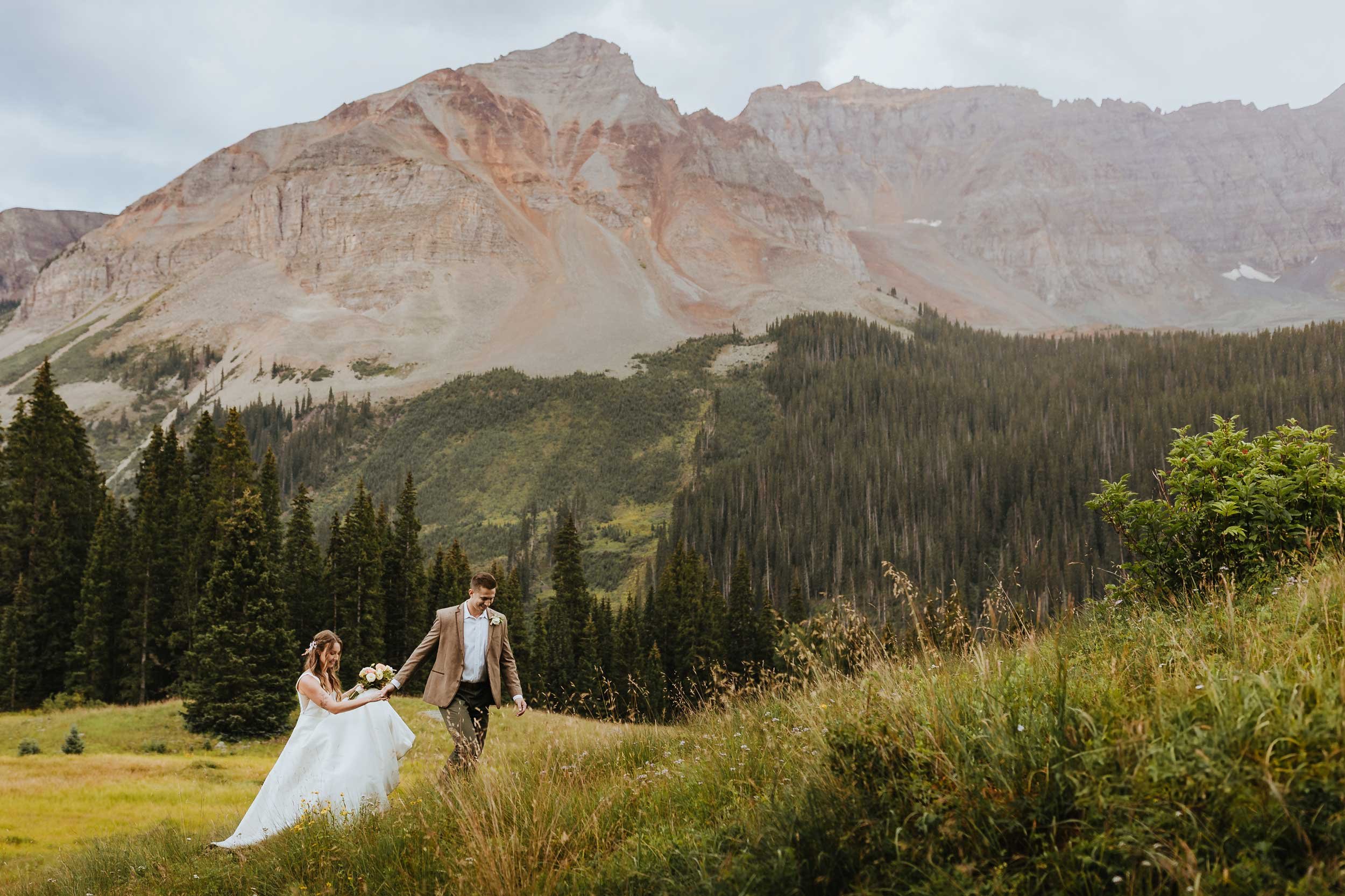 Bride and groom walking hand in hand through a grassy mountain meadow during their Telluride elopement