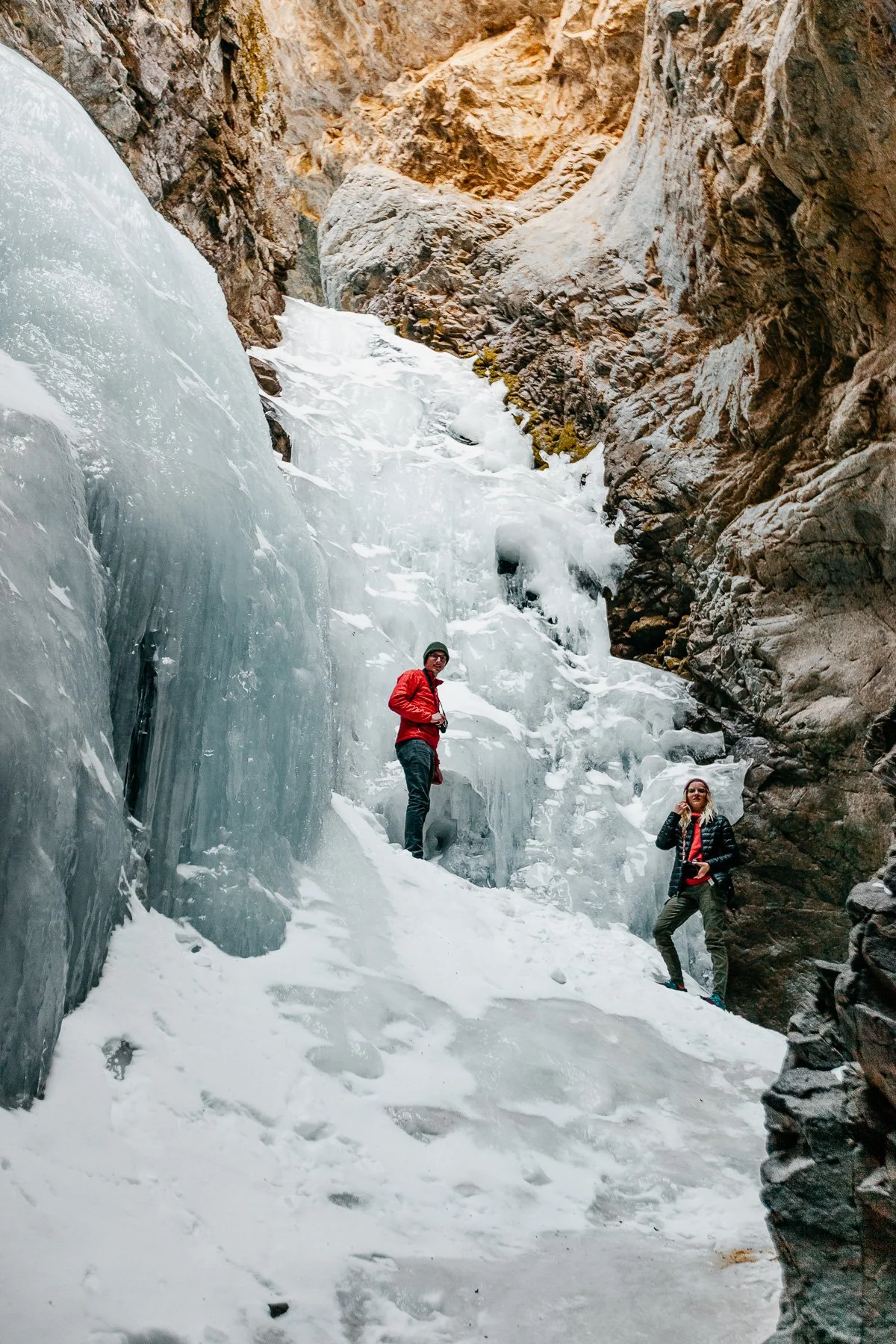 Two people in red jackets stand at the base of frozen Zapata Falls near Great Sand Dunes National Park