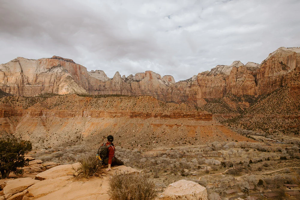 Hiker sitting on a rocky ledge overlooking a vast canyon
