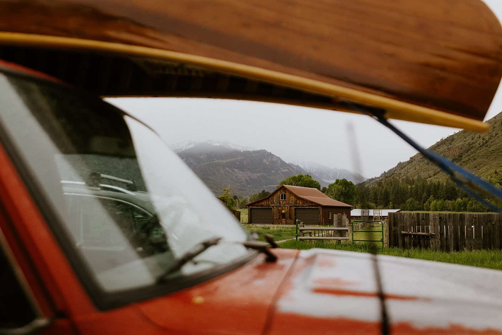 A view of a barn and the San Juan mountains through a red Land Cruiser with a canoe on top