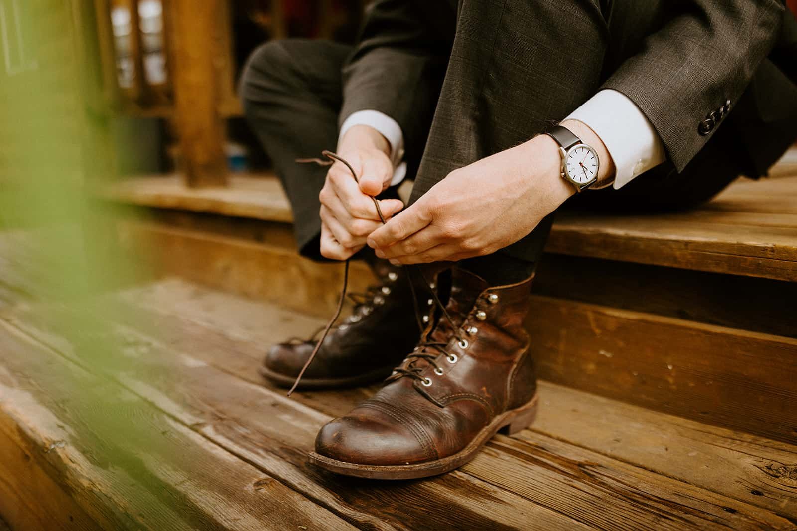 A man ties his Redwing boots on a wet porch