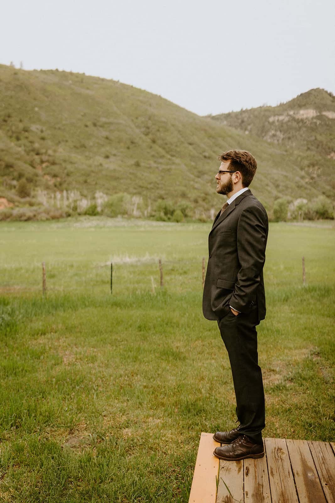 A man stands outside in a field waiting for a first look on his wedding day